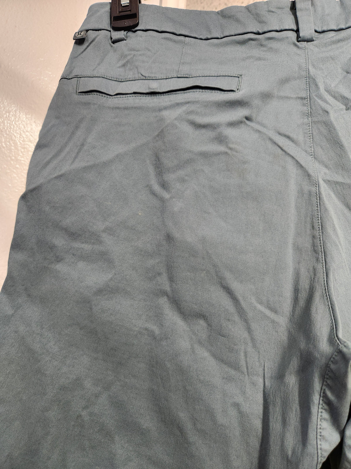 Close-up of the back waistband and pocket area of slate blue-gray chino pants, showing fabric texture, belt loops, and a dark belt buckle.