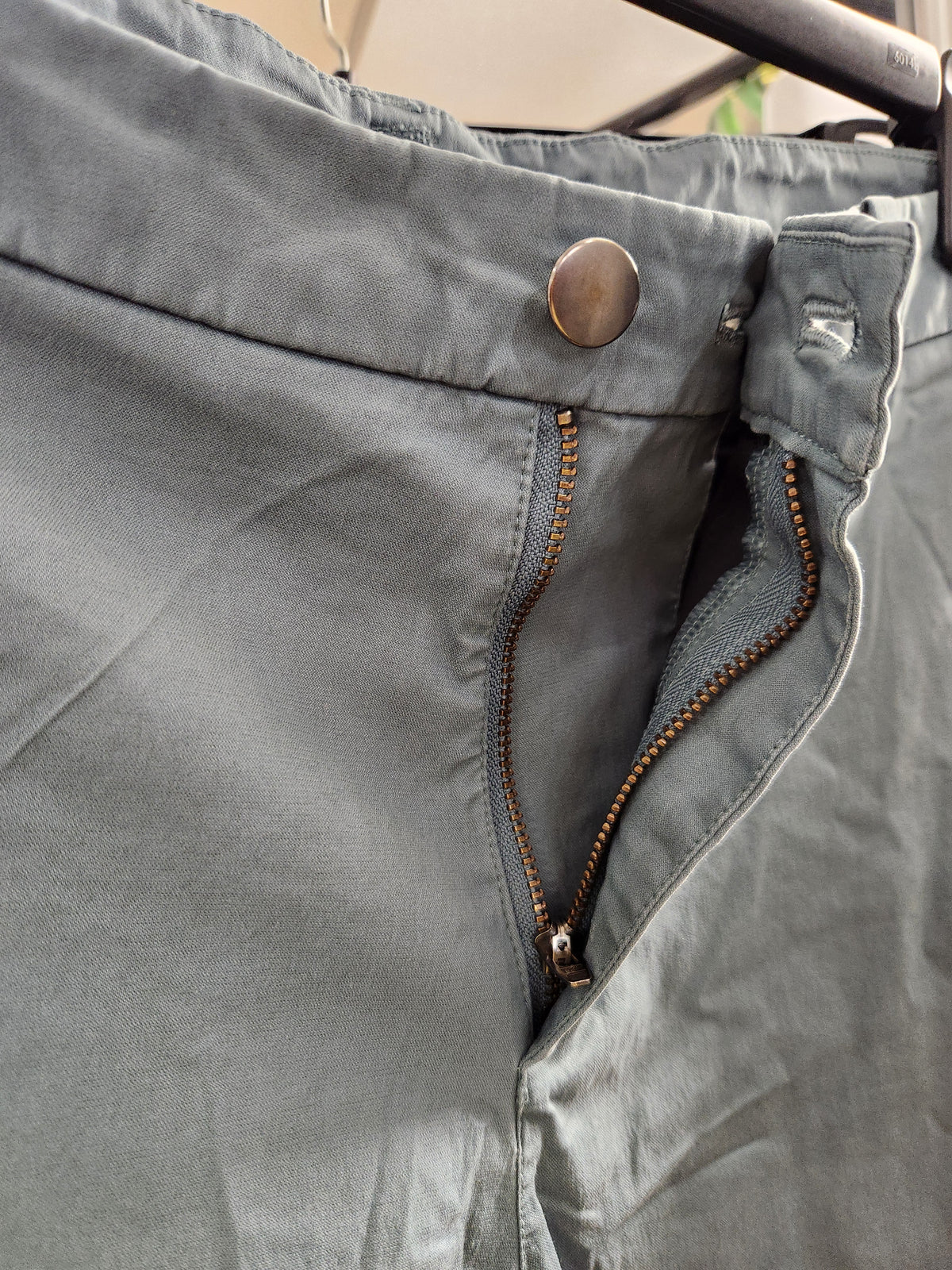 Close-up of a pair of gray pants showing the waistband, a metal button, and a partially unzipped front pocket with brown zipper teeth.