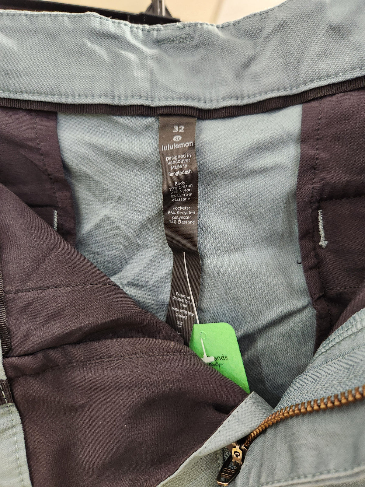 Close-up of the inner neck area of a jacket showing a gray and dark brown quilted lining, a brown size and brand tag reading '32 Subtlemag' (Subtlety), and a bright green paper tag.