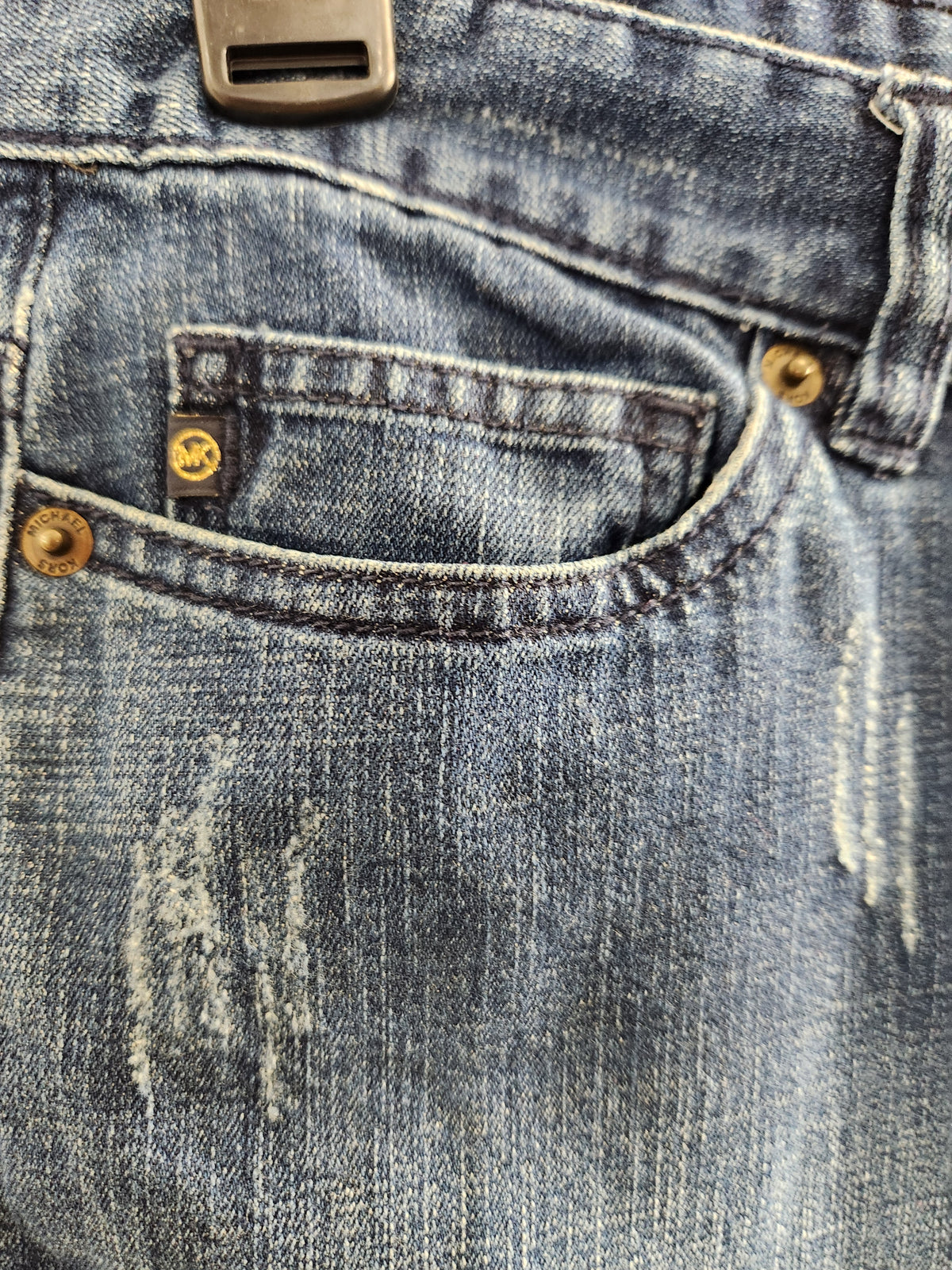 Close-up of the back pocket of light-wash blue denim jeans with brass-toned rivets and a small yellow brand tab.