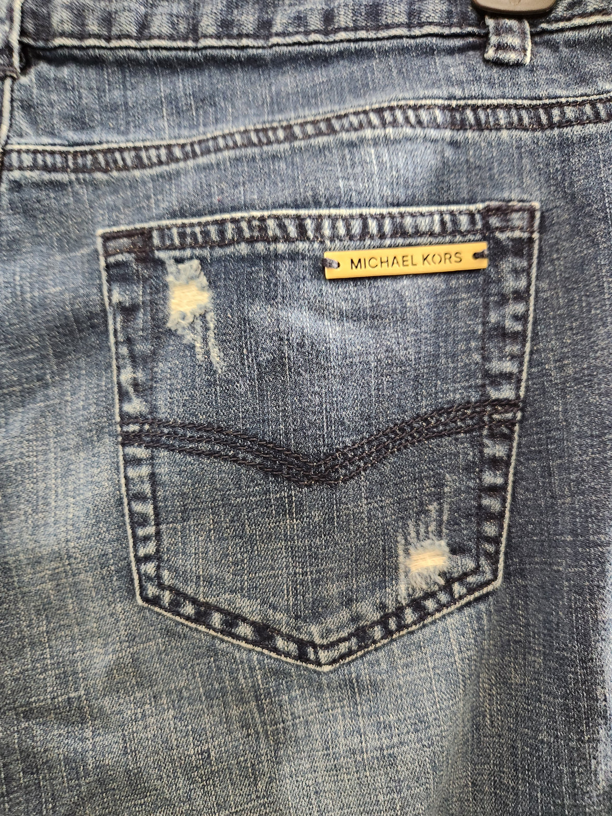 Close-up of the back pocket of distressed blue denim jeans with a yellow Michael Kors brand tab.