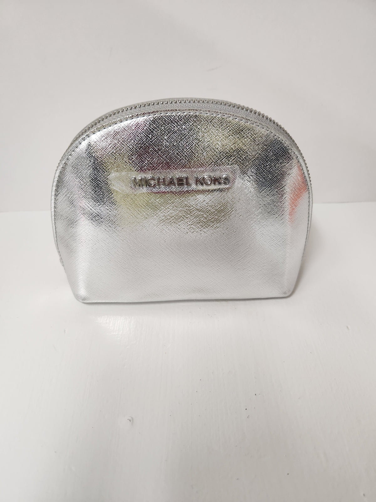 A Michael Kors metallic silver zippered cosmetic pouch with a silver-tone logo plaque on the front, set against a plain white background.
