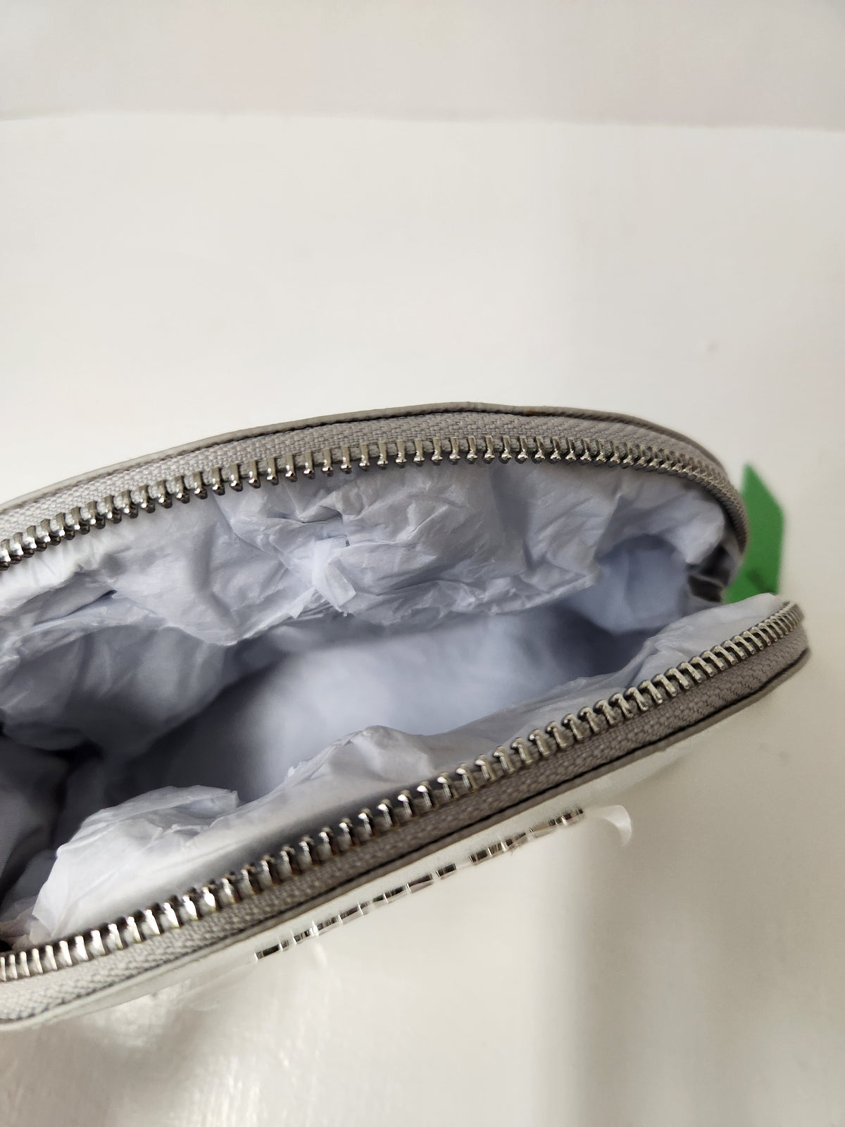 A close-up of a silver zippered pouch or small bag shown open, revealing a light gray interior lining with crumpled tissue paper inside. The zipper is metallic silver, and a small portion of a white exterior is visible along the bottom edge.