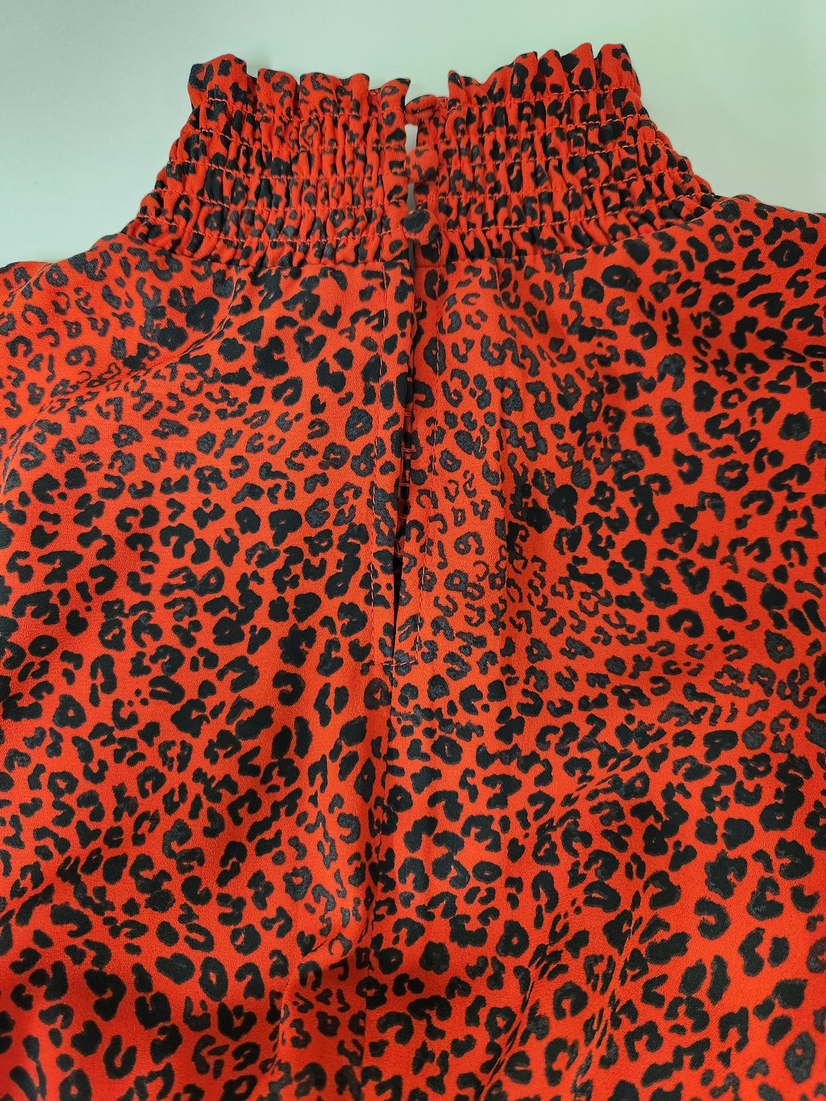 Close-up of a red and black leopard print garment with a gathered, smocked high neckline.
