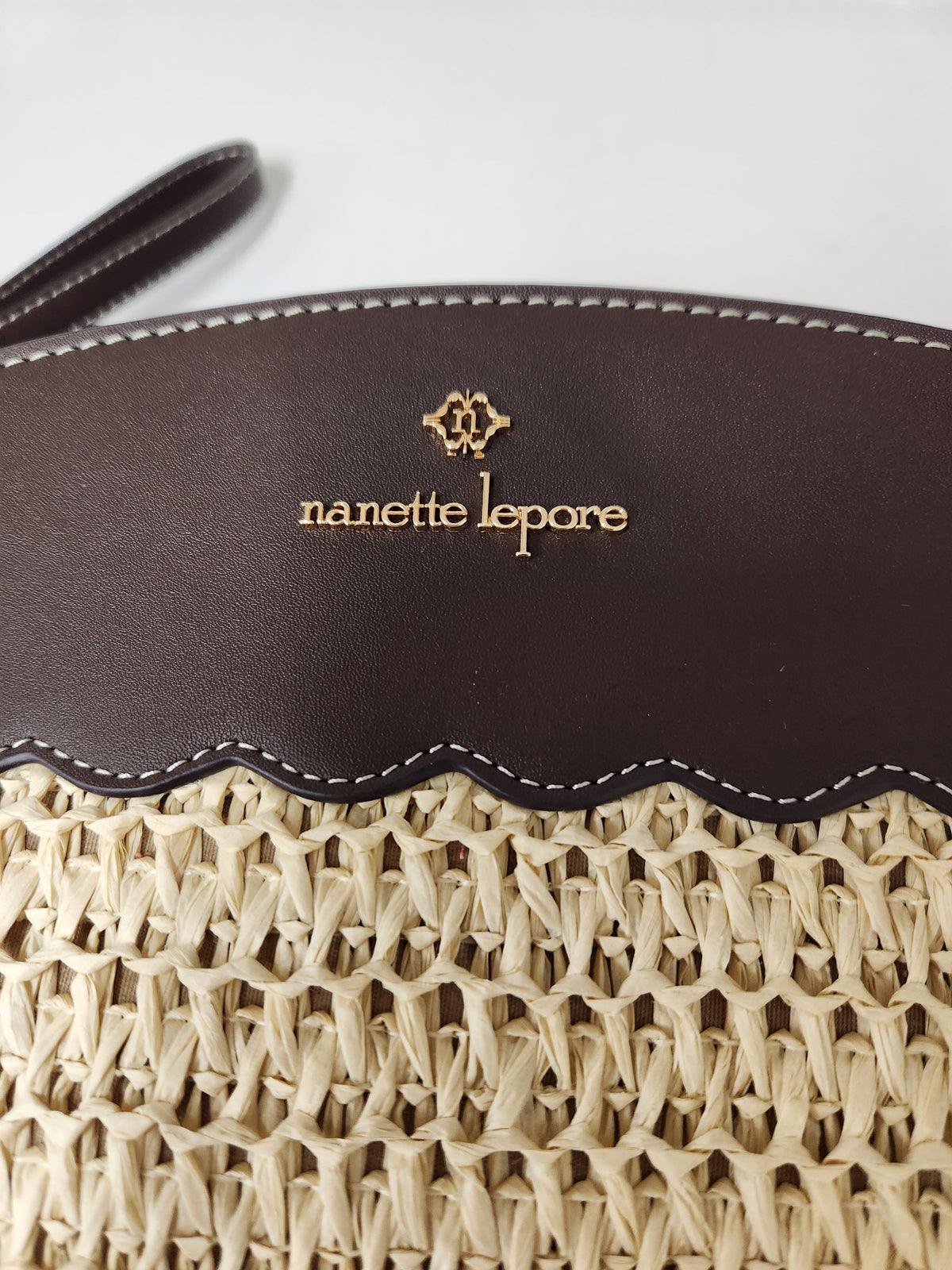 Close-up of a woven straw bag with a dark brown leather top panel featuring the gold-embossed 'nanette lepere' logo and brand name.