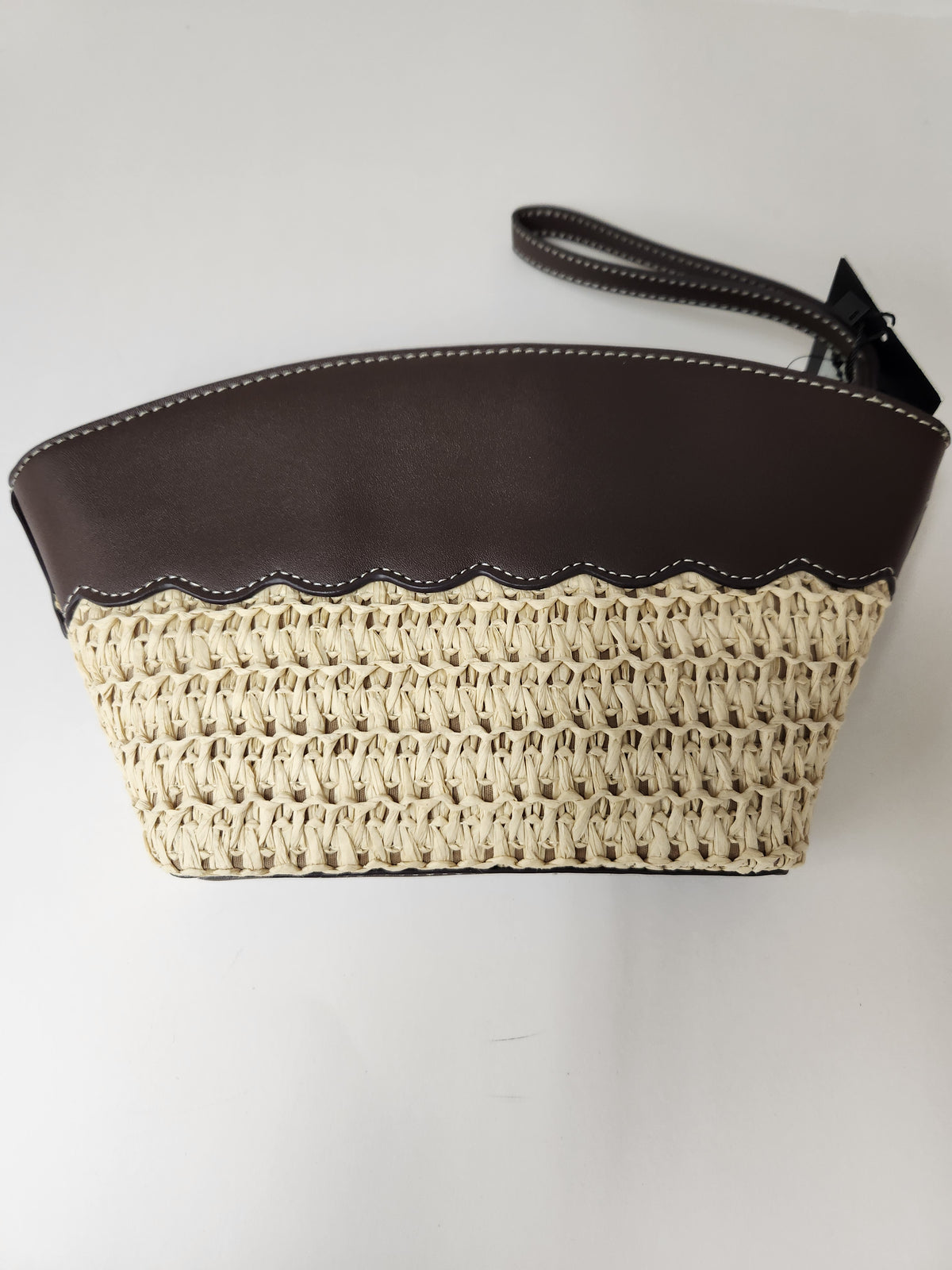A small handbag with a dark brown faux-leather top section and a cream-colored woven straw lower section, featuring a dark brown wristlet strap.