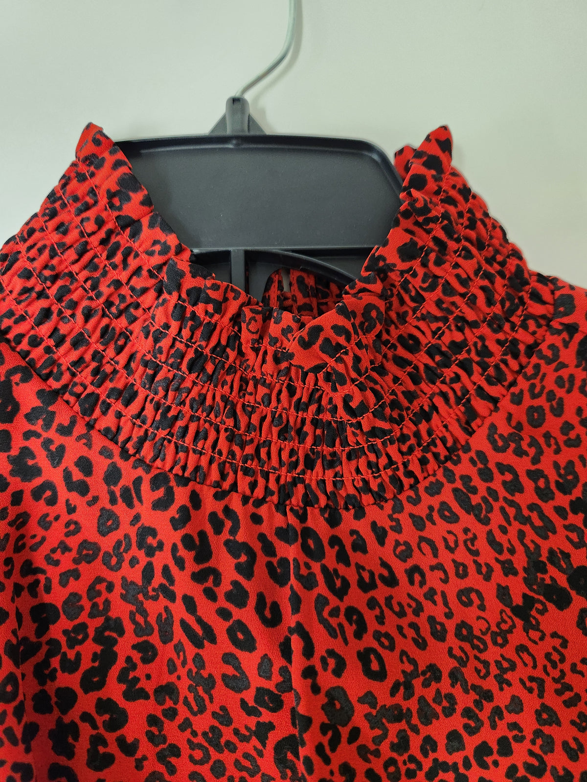 A close-up of a red and black leopard print blouse on a black hanger, featuring a smocked high neckline.