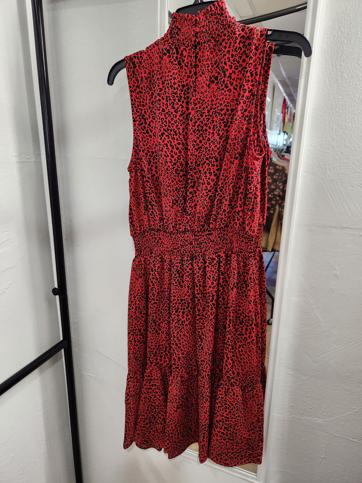 A sleeveless red dress with a black leopard print pattern, hanging on a black hanger in front of a white wall.