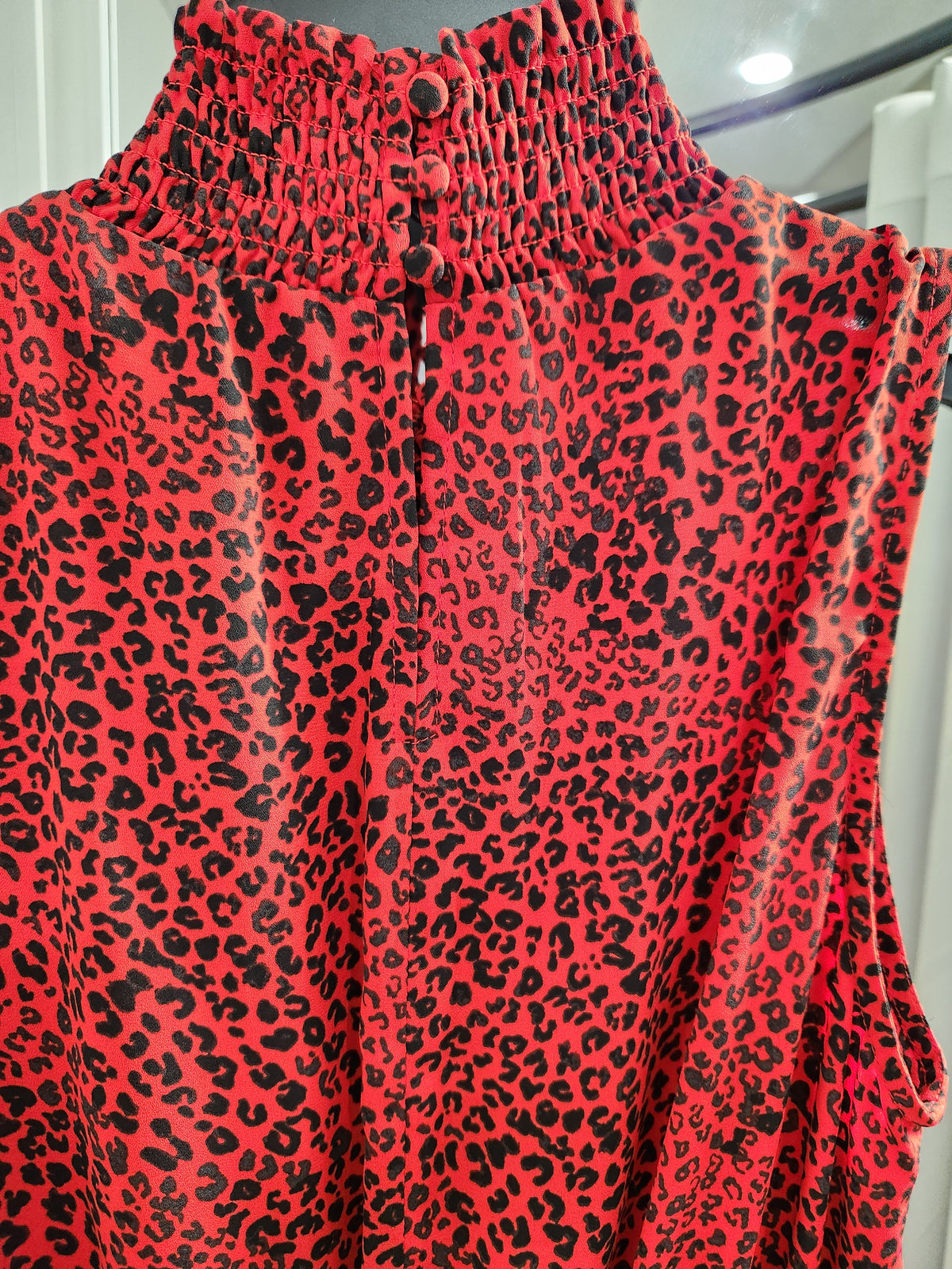 A sleeveless red top with a black leopard print pattern, featuring a high smocked collar and a buttoned front placket.