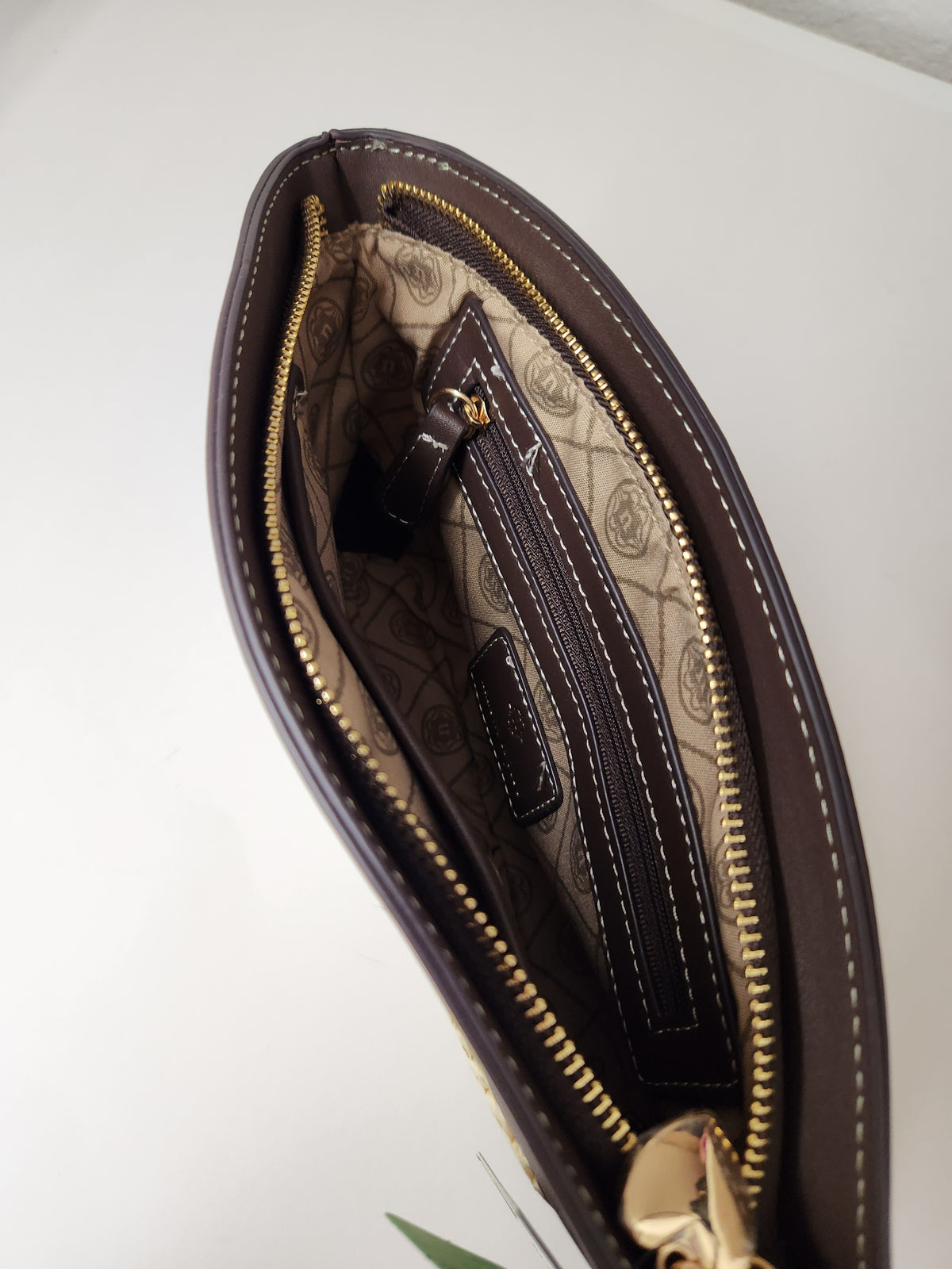 Close-up of an open dark brown leather clutch or wallet showing a beige patterned interior lining with gold-tone zippers and stitching.