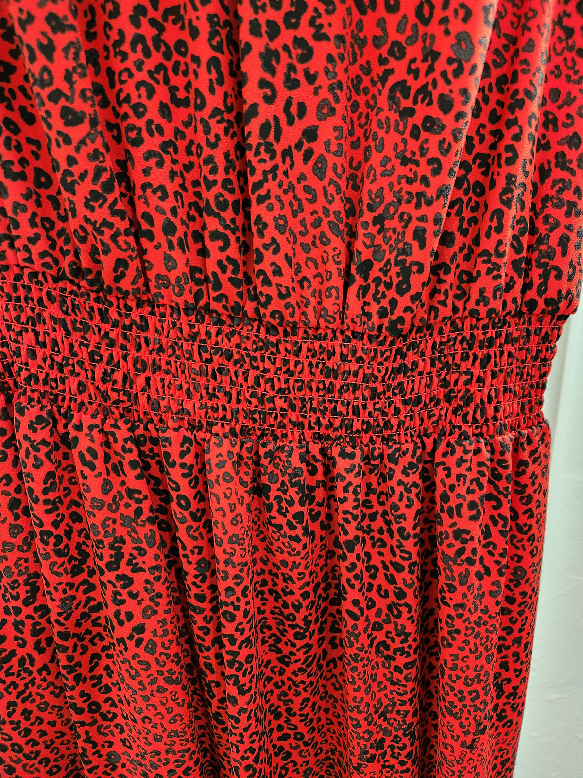 Close-up of a red leopard print fabric with a smocked waistband, showing the texture and pattern details.