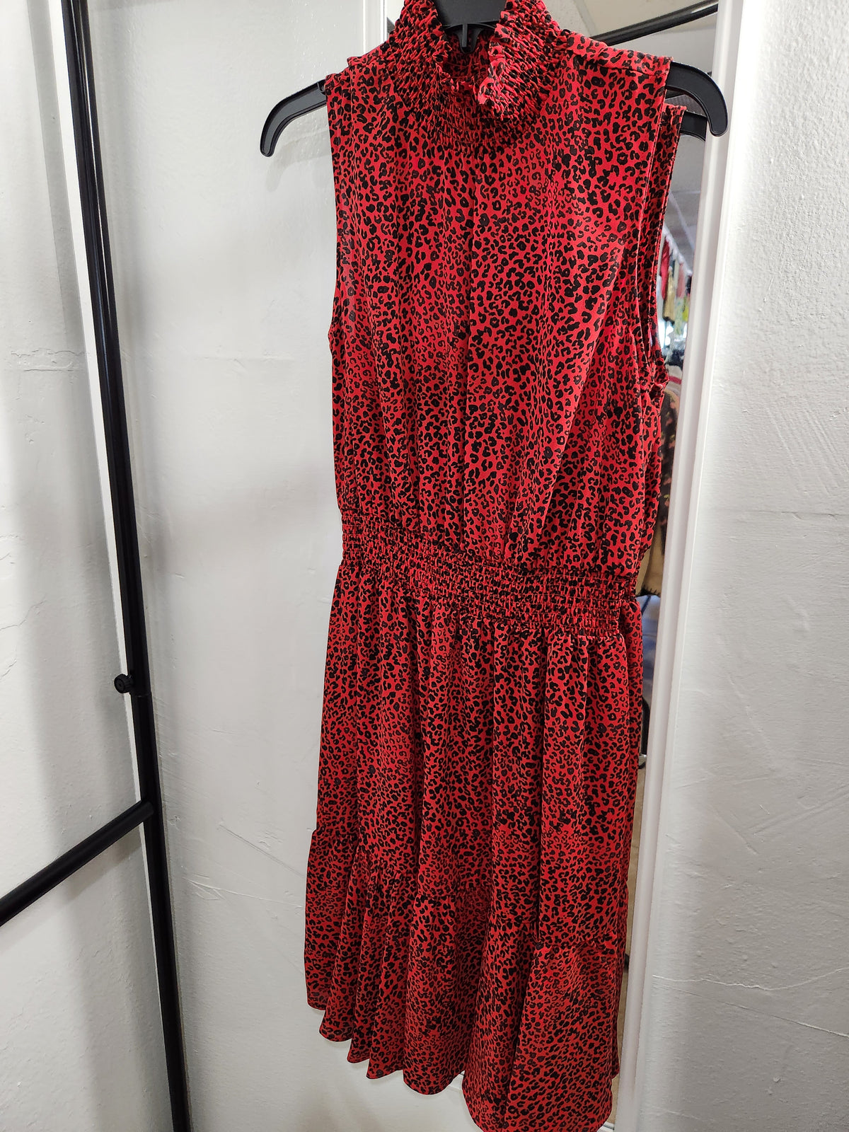 A sleeveless high-neck red dress with a black leopard print pattern, hanging on a black hanger against a white wall.
