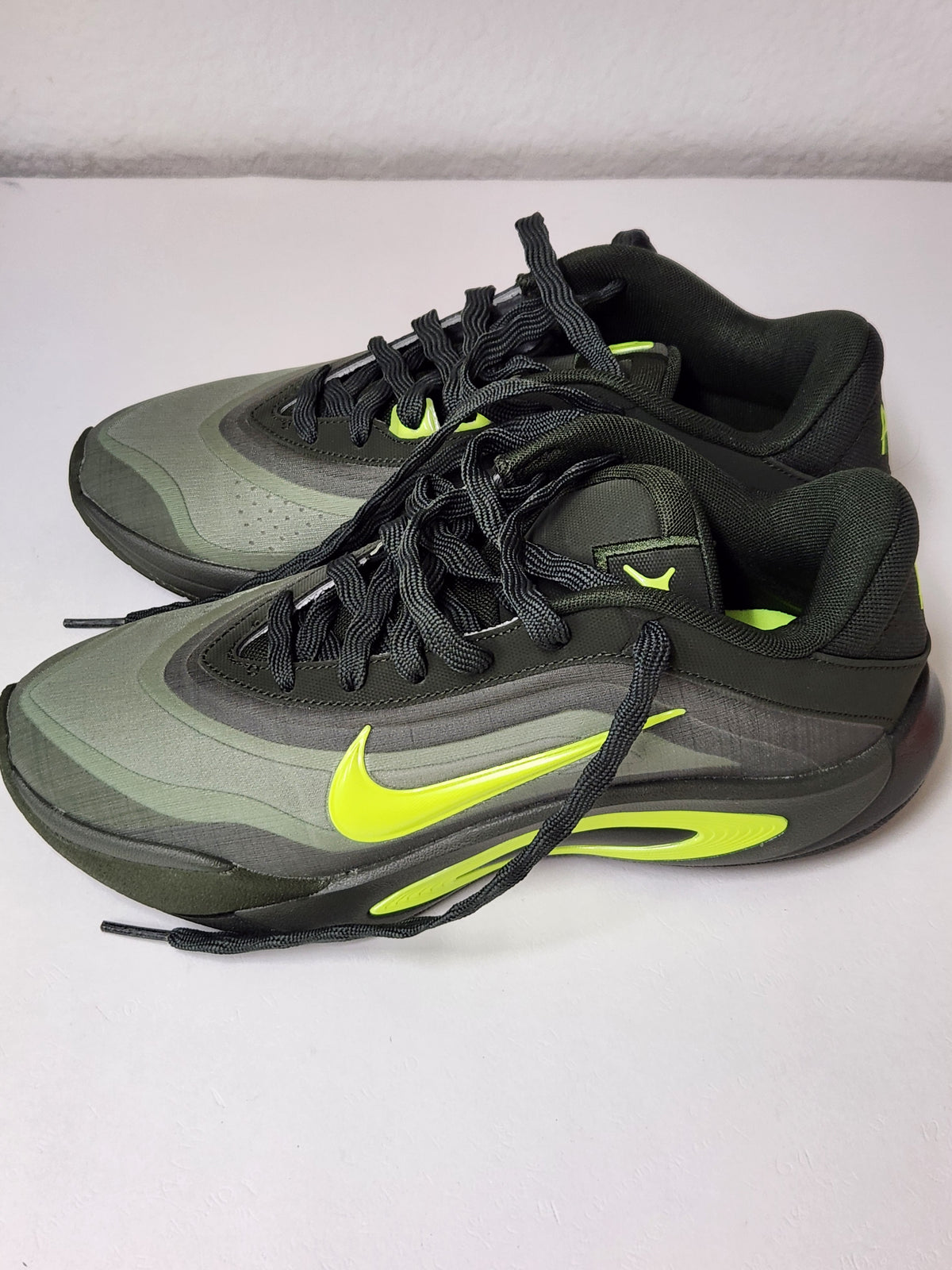 A pair of Nike athletic sneakers in dark gray and black with bright neon yellow-green accents, including a prominent Swoosh logo and matching details on the tongue and midsole.