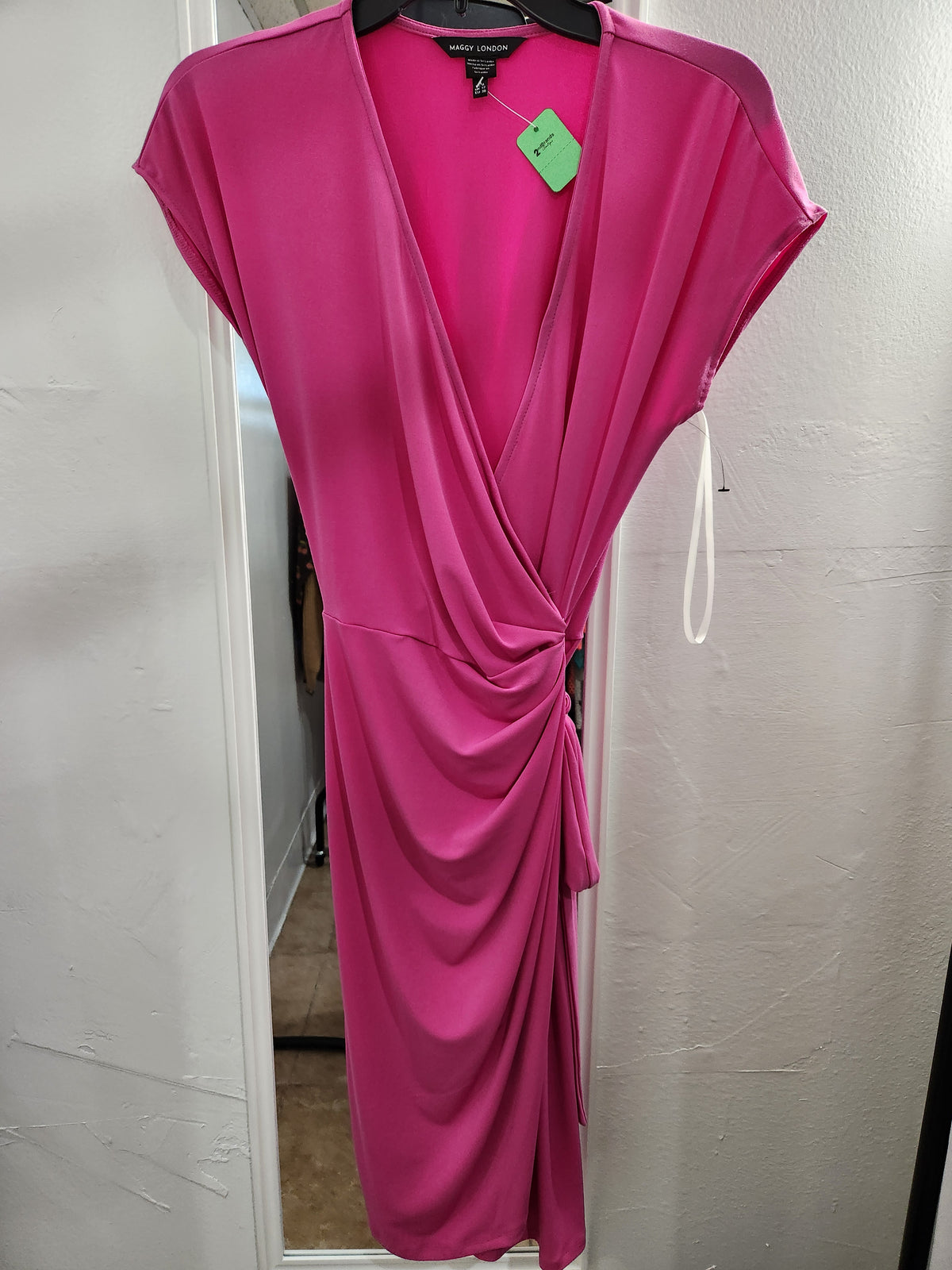 A bright pink wrap-style dress with cap sleeves and a side tie detail, hanging on a black hanger against a white door frame.
