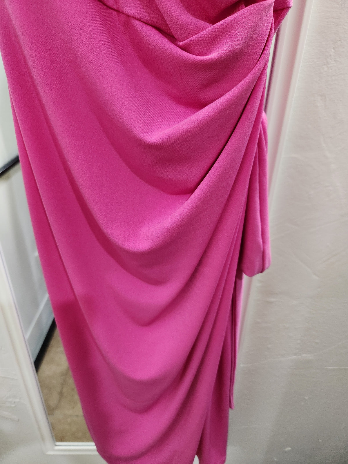 A draped bright pink fabric garment or dress shown close up against a light-colored wall and doorway.