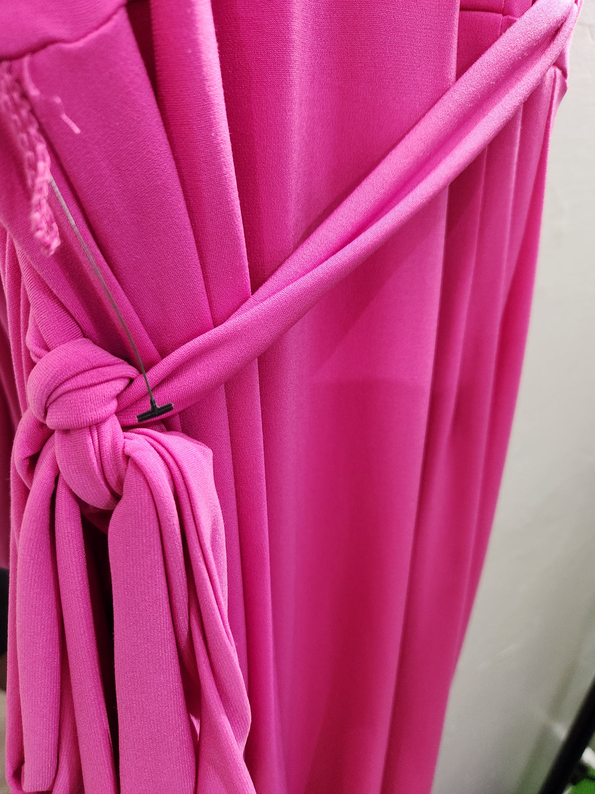 A close-up of a bright pink fabric accessory, likely a dress or wrap, tied in a knot with a small black clip to show the material and texture.