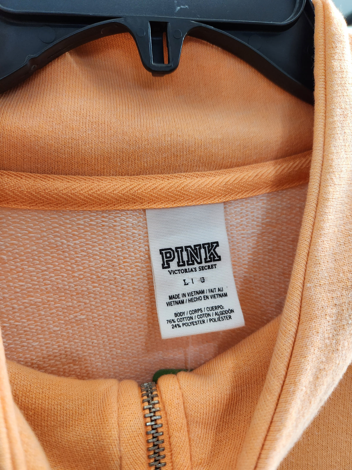 Close-up of a peach-colored zip-up hoodie on a black hanger, showing the inner neck label which reads 'PINK VICTORIAS SECRET' and size 'L 8'.