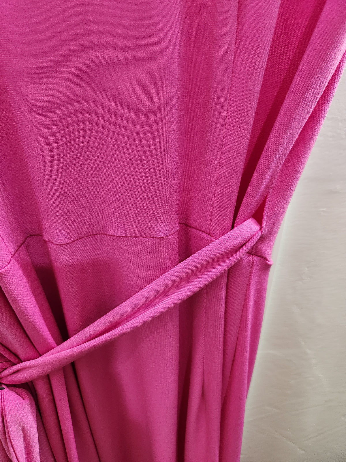 A close-up of bright pink draped fabric tied back with a matching tie, showing the material texture and folds against a light neutral background.