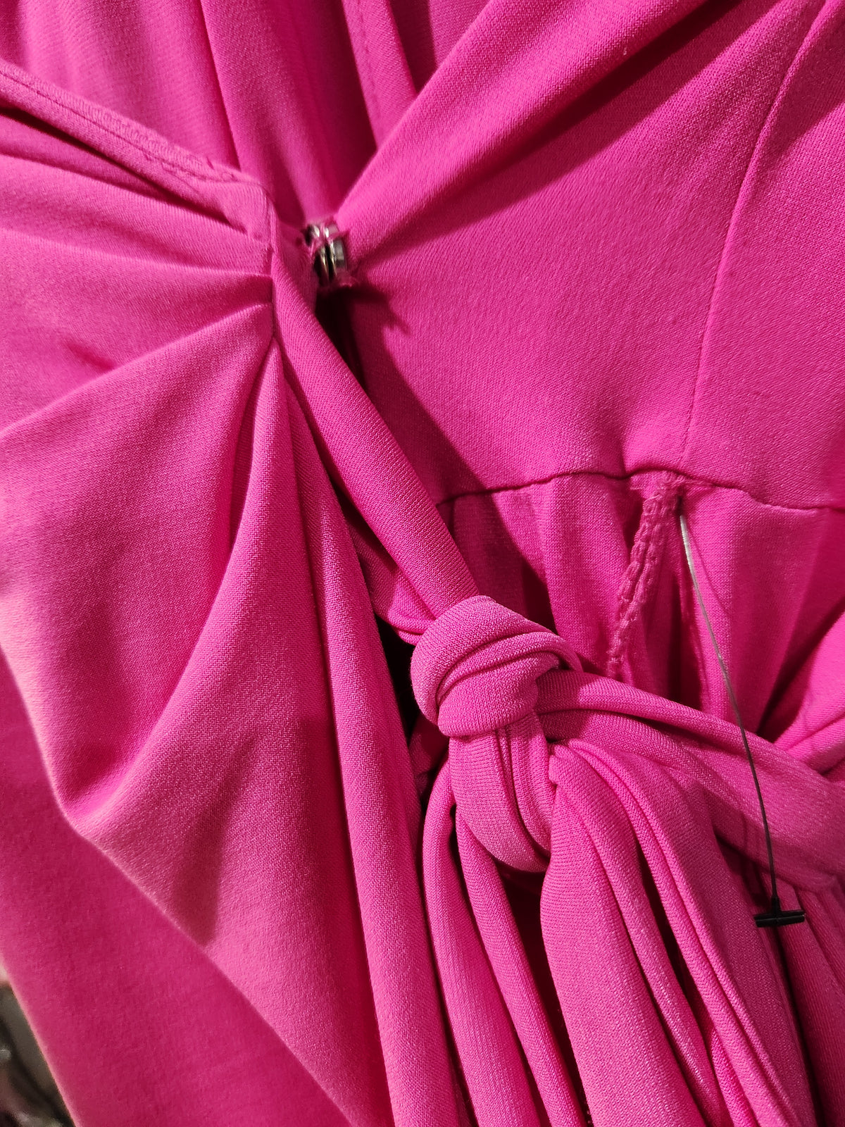 A close-up of bright pink fabric with a gathered waist tie and a small metal ring closure, photographed tightly with no person or environment visible.