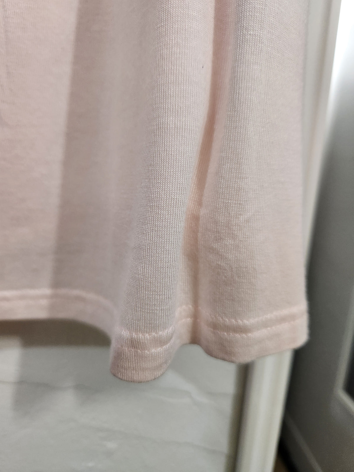 Close-up of a light pink ribbed knit garment, showing the fabric texture and hem detail.