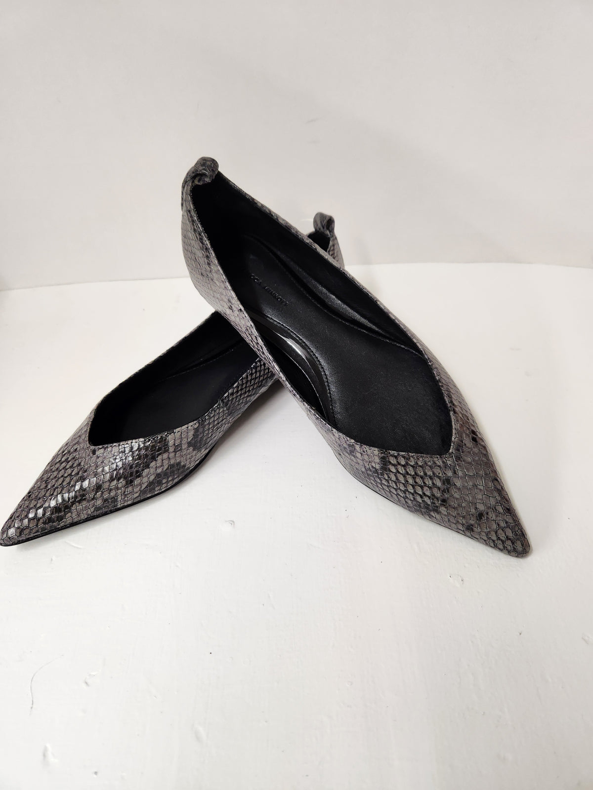 A pair of pointed-toe flats with a metallic silver and black snakeskin pattern, photographed on a white surface against a white background.