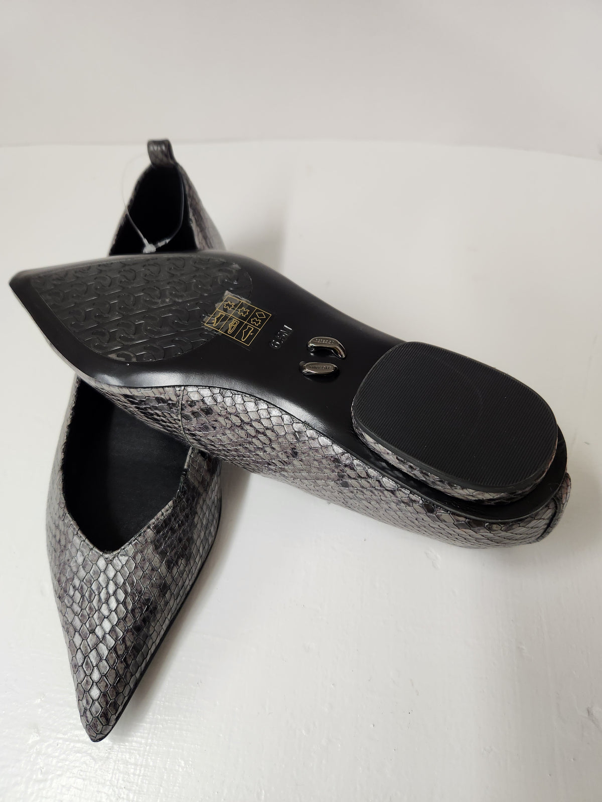 A pair of pointed-toe flats with a gray and black snakeskin pattern, displayed on a white surface with one shoe showing its black sole and the other showing its side profile.