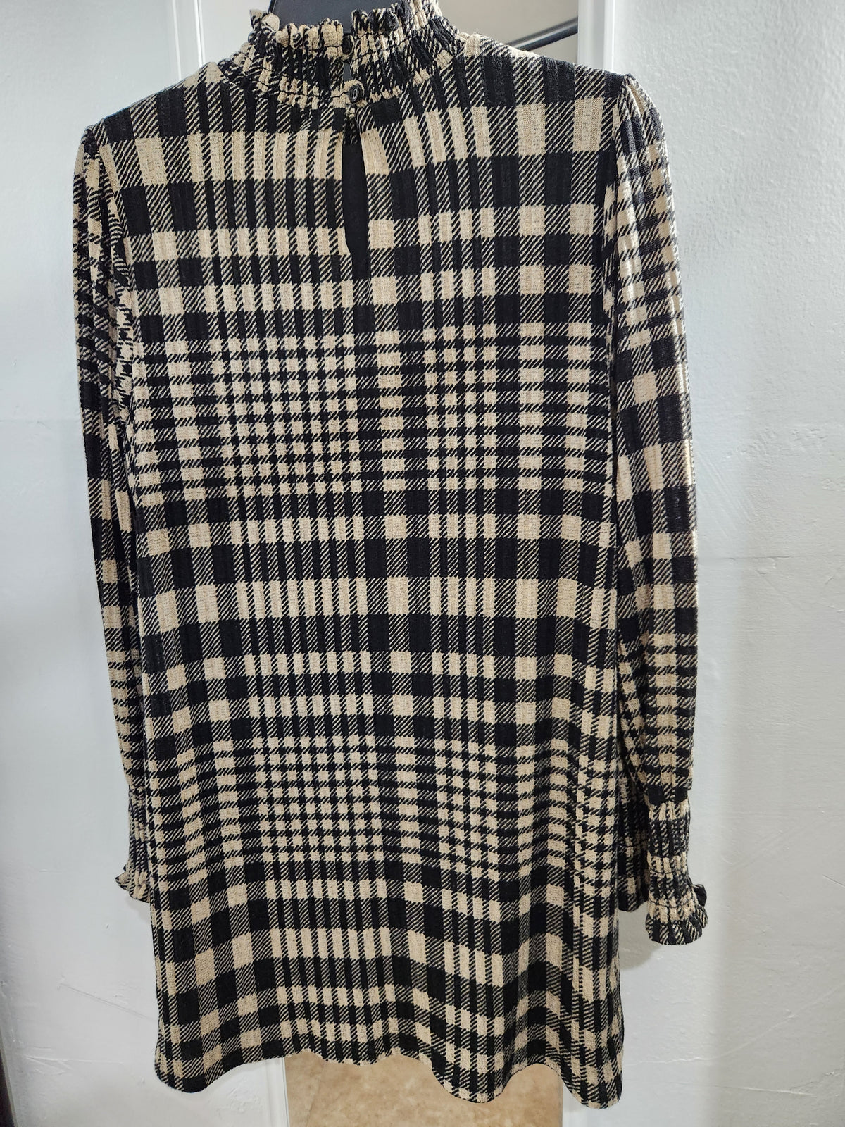 A long-sleeve plaid tunic top with a high gathered mock neck and elasticized cuffs, shown on a dress form against a white wall.