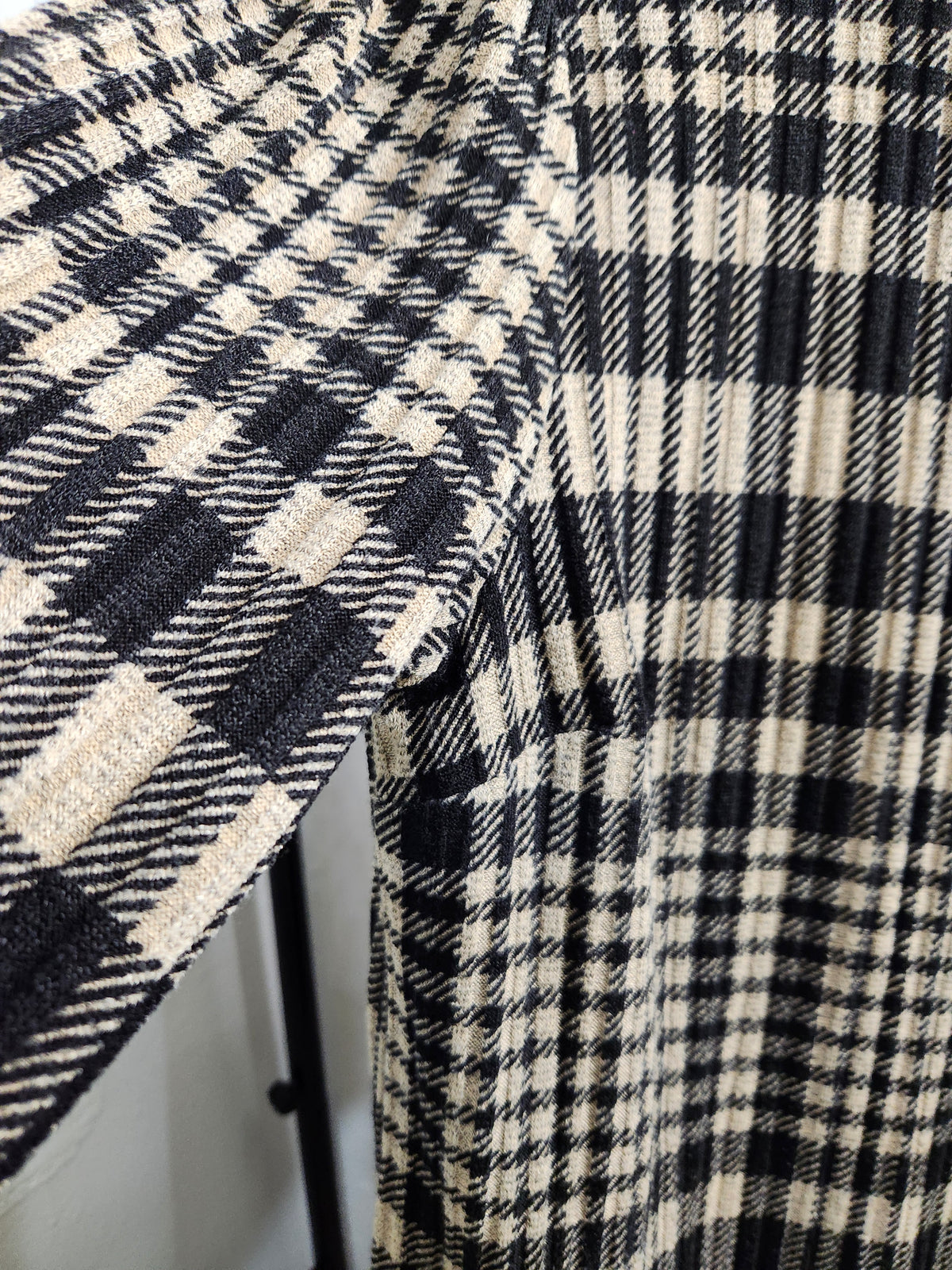 Close-up of a black and off-white plaid fabric garment, showing the textured woven pattern and folded sleeve detail.