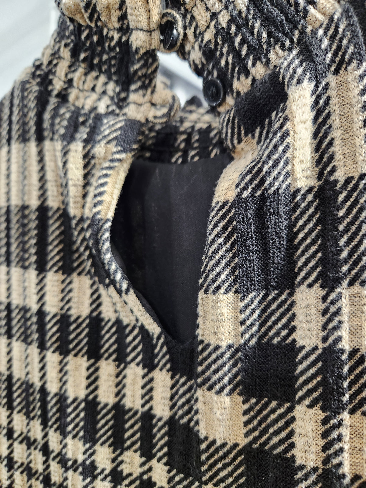 Close-up of a black and beige plaid fabric garment, showing the textured woven pattern and a black inner lining.