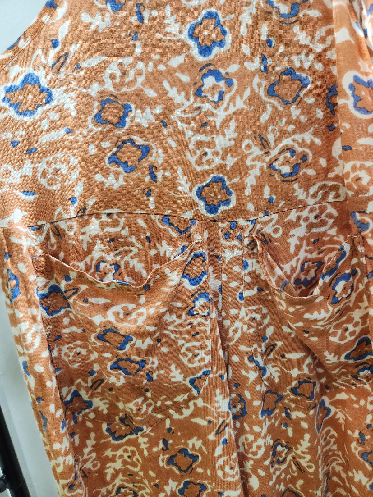 A close-up of a patterned garment, likely a dress, featuring a rust-orange base with blue and cream floral and abstract motifs.