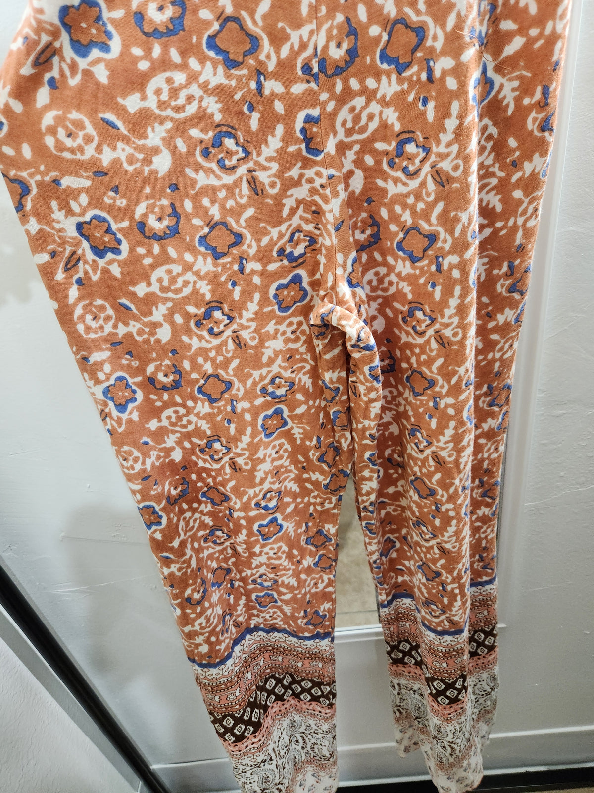 Patterned leggings in terracotta orange with blue and white abstract floral motifs and a decorative multicolor lace-like hem.