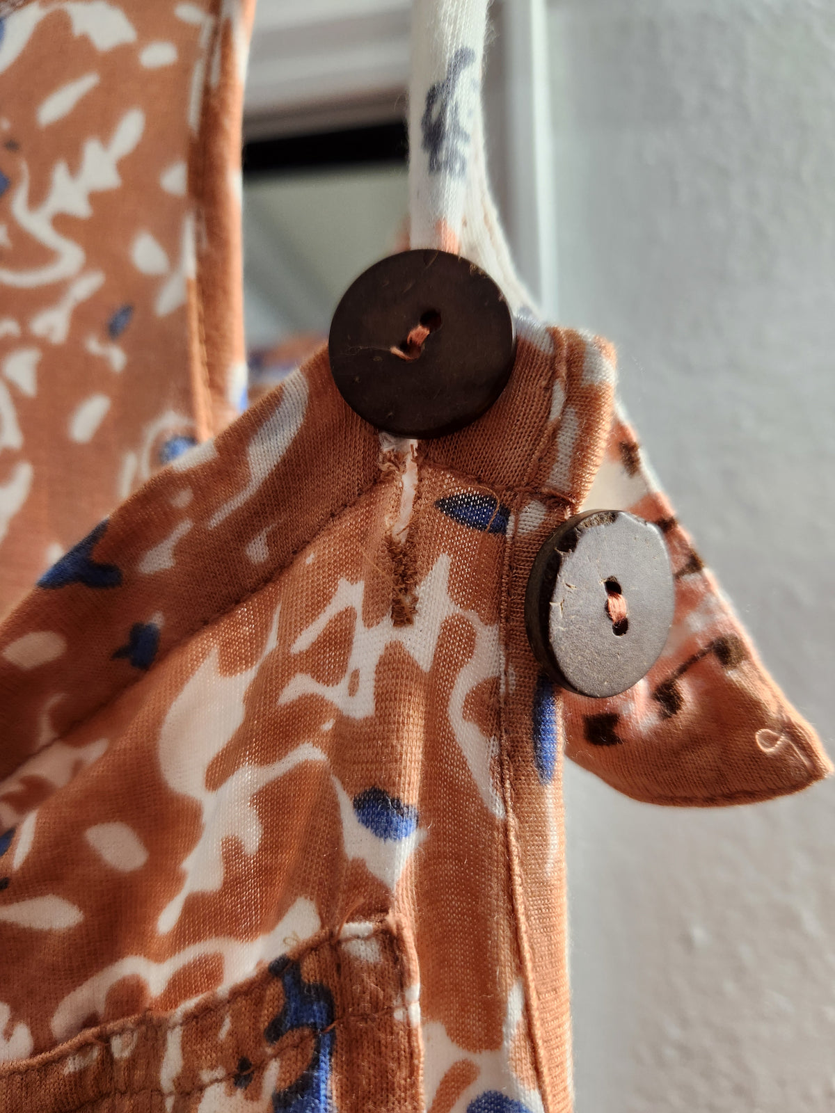 Close-up of a patterned fabric bag or garment featuring a brown and cream abstract print with blue accents, detailed with two dark wooden buttons.