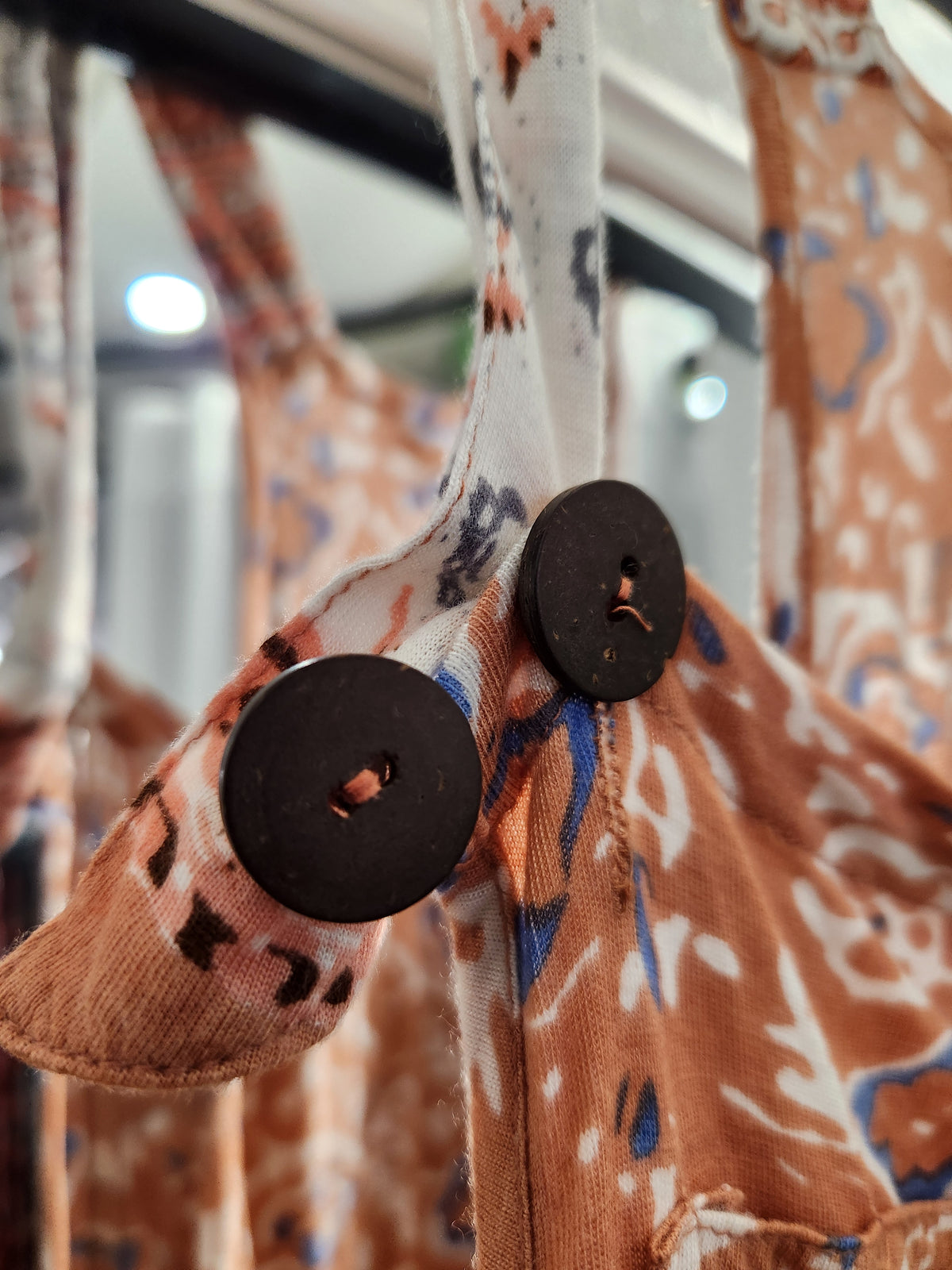 Close-up of a patterned garment with two large dark brown buttons, featuring a rust-orange, white, and blue abstract print.