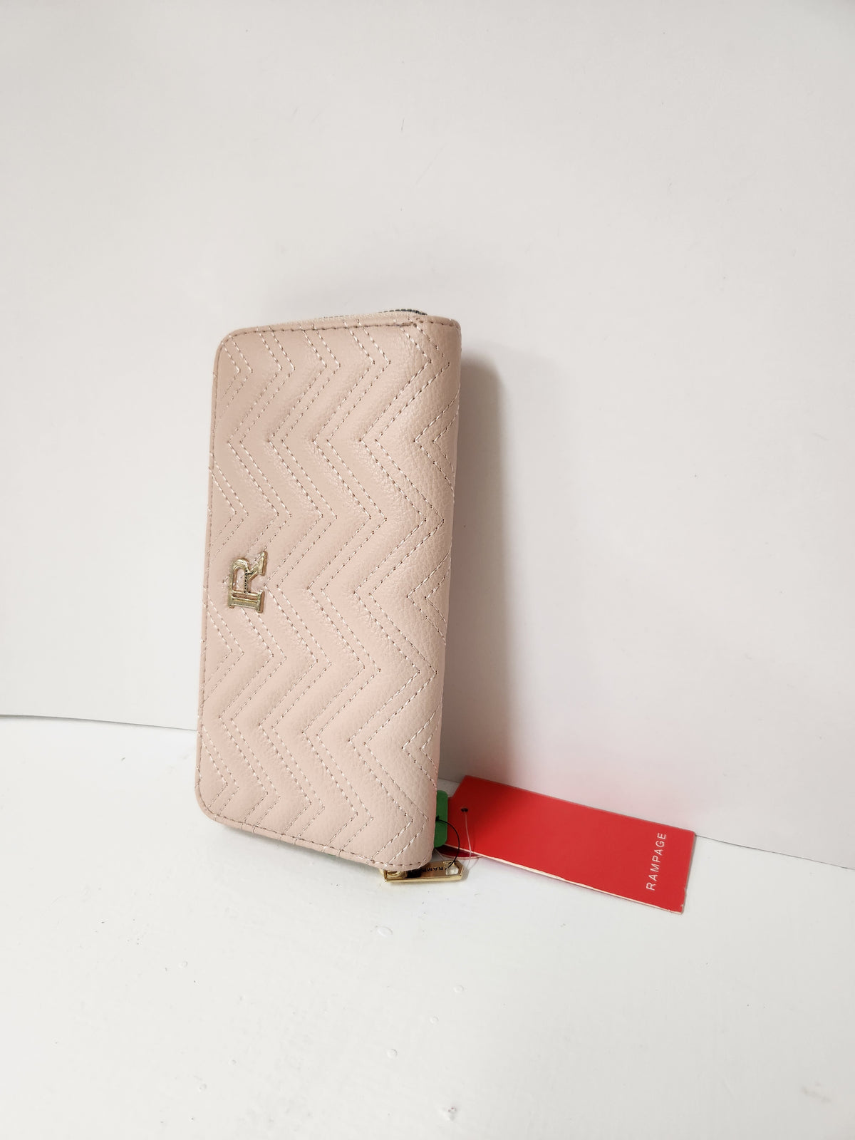 A light pink quilted zip-around wallet with a gold-tone logo clasp, standing upright next to its red brand tag on a white surface.