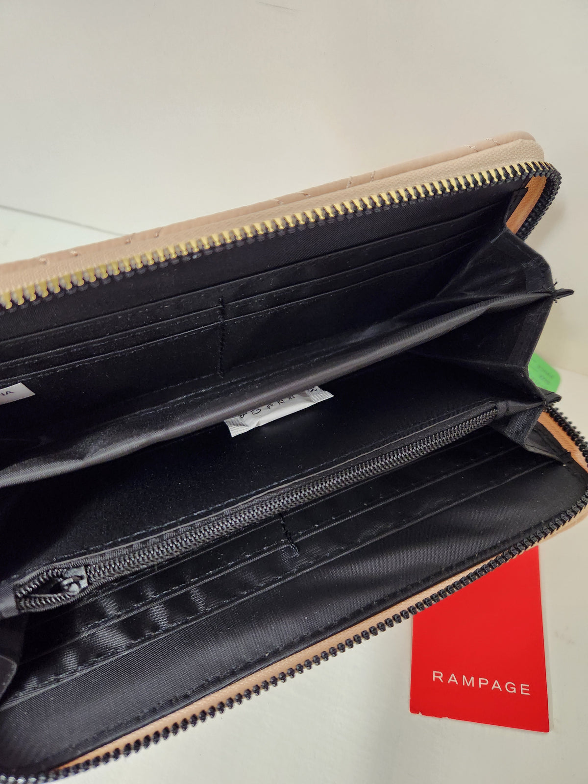 An open beige and black zip-around wallet with multiple interior card slots and a red Rampage brand tag visible on a light surface.