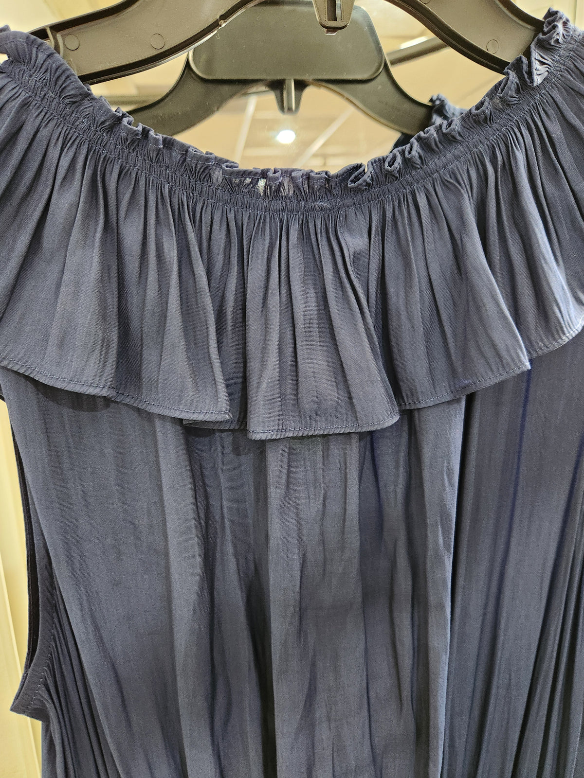A close-up of a slate blue off-the-shoulder blouse with a ruffled neckline, hanging on a black hanger.