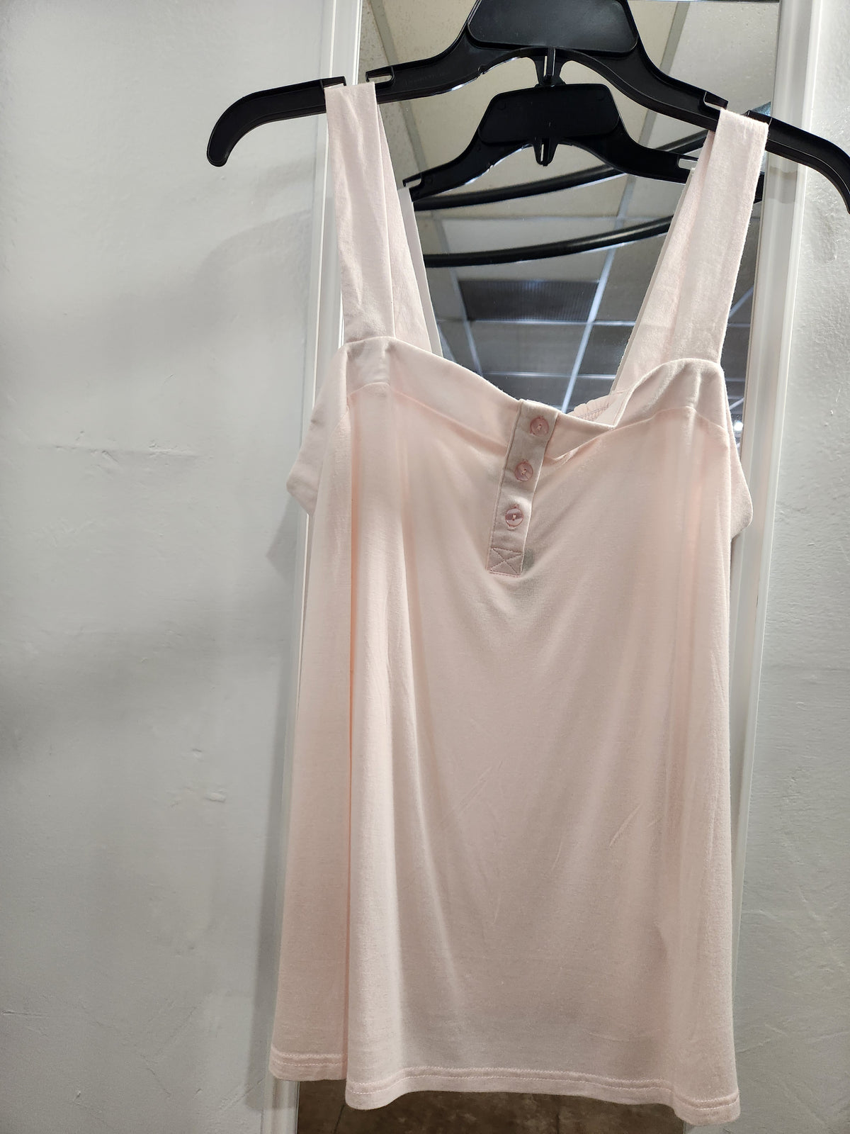 A light pink sleeveless henley tank top with a three-button placket, hanging on a black hanger against a white wall.