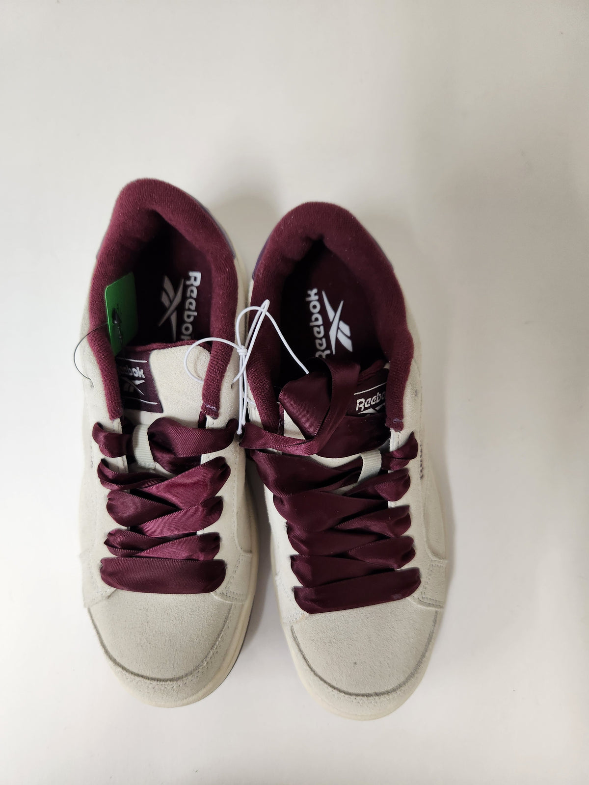 A pair of Reebok sneakers with off-white suede uppers and deep burgundy laces and lining, shown from a top-down view on a plain white background.
