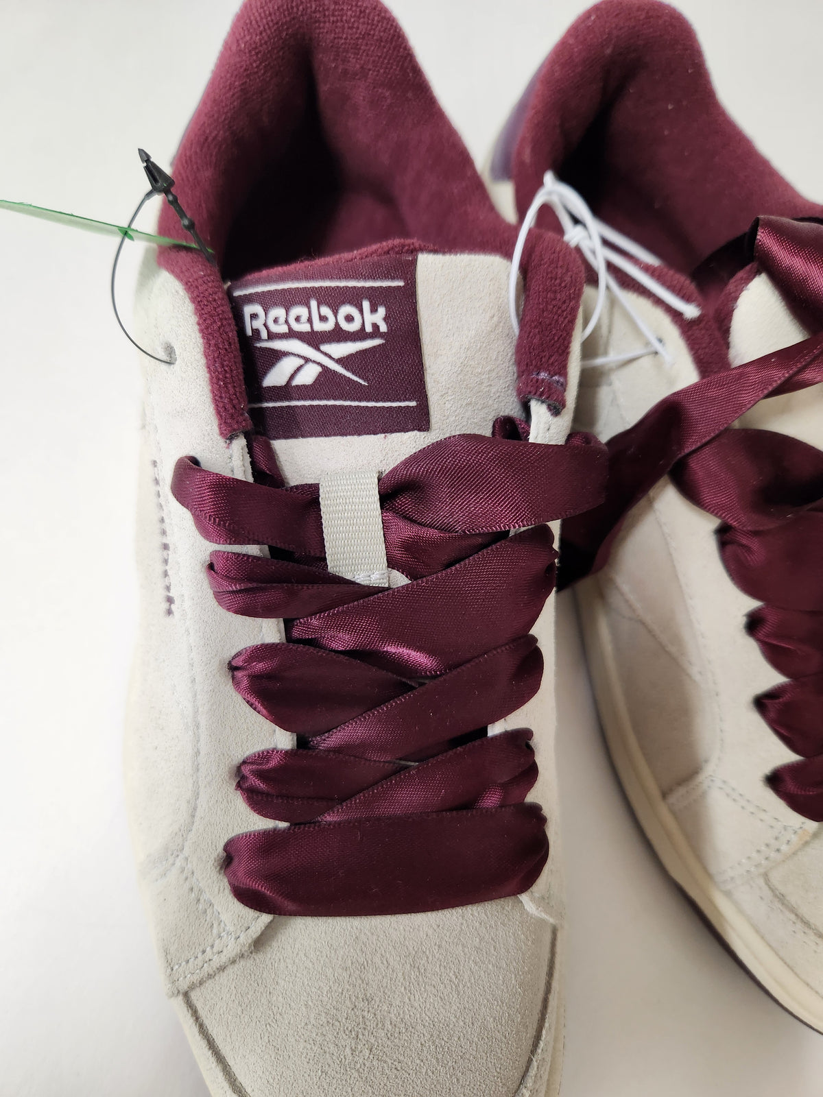 A pair of Reebok low-top sneakers in off-white suede with deep burgundy satin laces and matching burgundy lining, shown on a plain light background.