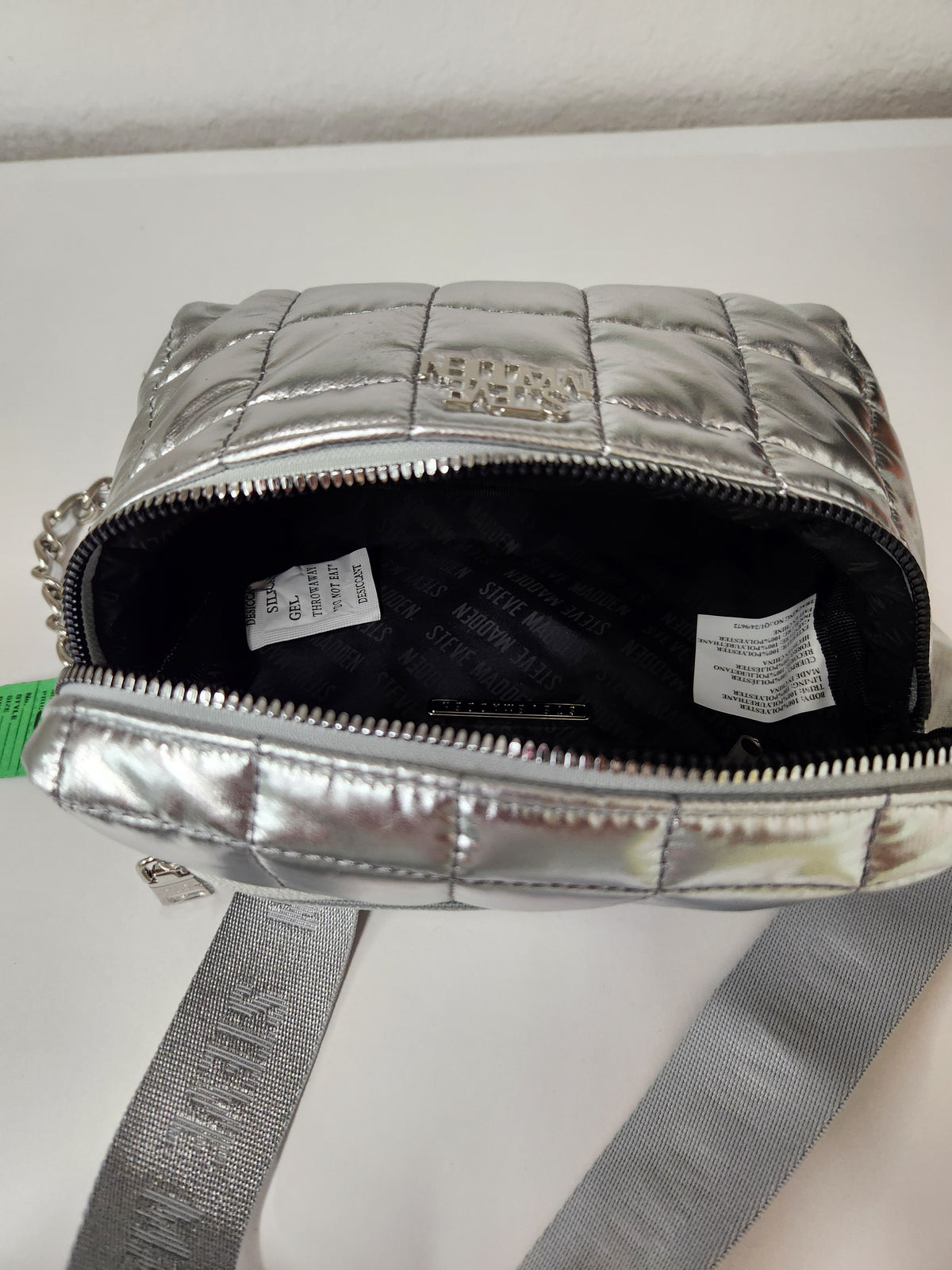 A silver metallic quilted crossbody bag with a black interior lining, shown open with its strap visible below. The brand name 'MARCY' is embossed on the front and printed on the interior labels.