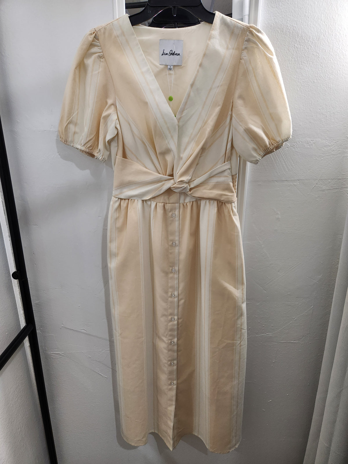 A cream-colored satin dress with puff sleeves, a V-neckline, and a front button-up, hanging on a black hanger against a white wall.