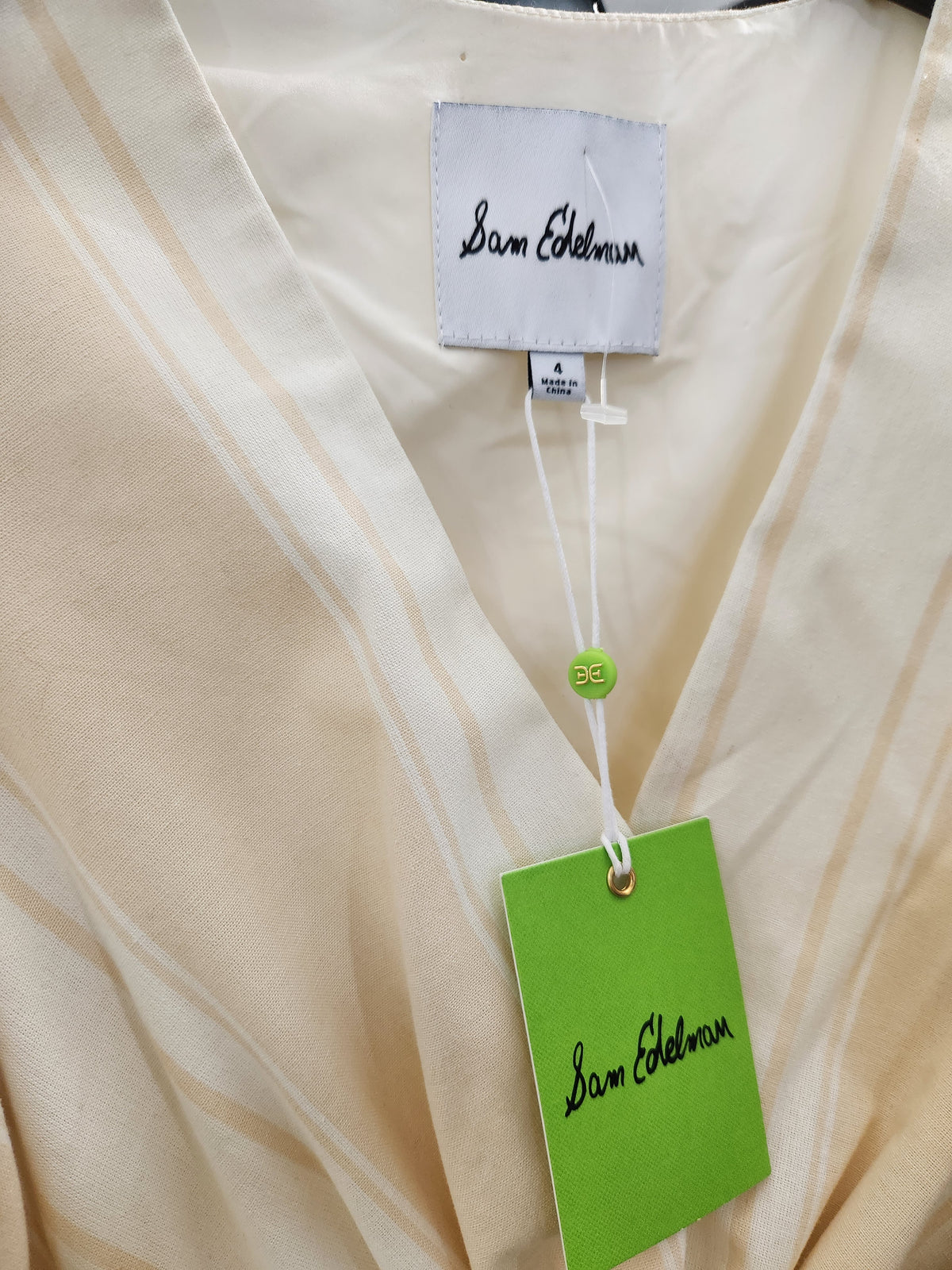 Close-up of a cream-colored Sam Helman garment with a white brand label and a bright green hangtag.