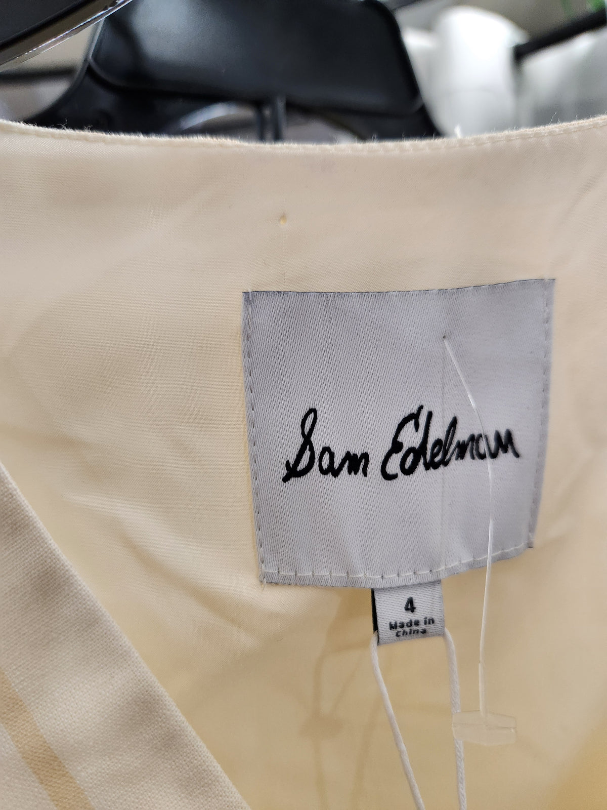 Close-up of a cream-colored garment's inner neck label, featuring a gray fabric patch with the brand name 'Sam Edelman' embroidered in black script.