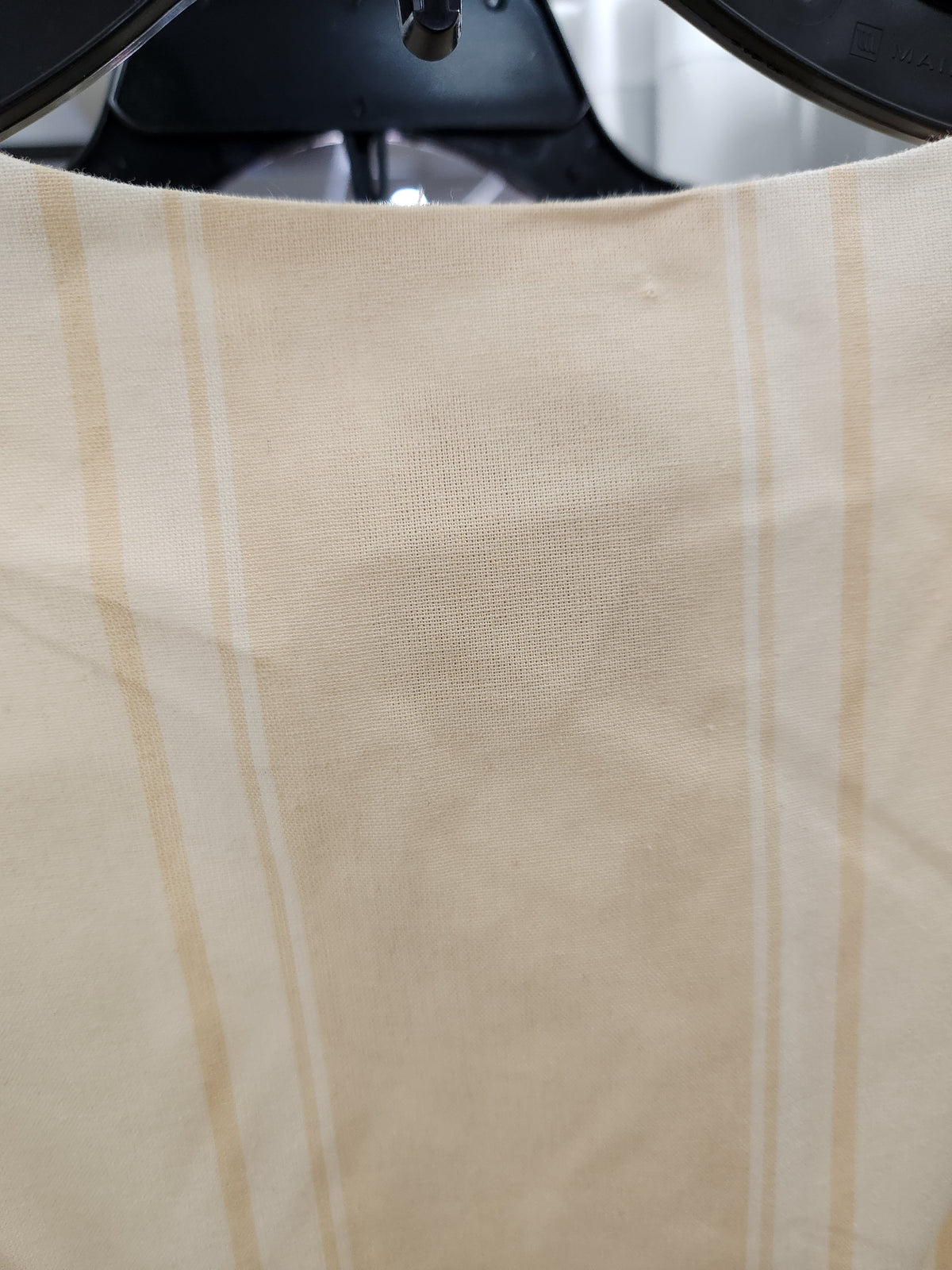 A close-up of a beige fabric with vertical white stripes, draped over a black hanger.