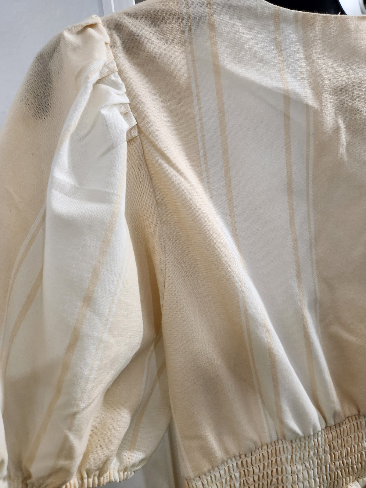 Close-up of a cream-colored blouse with vertical tan stripes, featuring a smocked waist and puffed sleeves.
