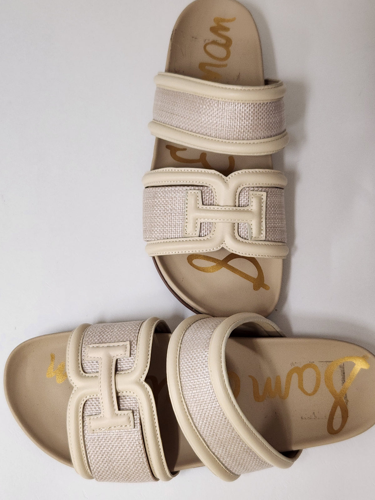A pair of beige slide sandals with wide woven straps and large interlocking 'H' hardware, shown on a plain light background. The insoles display the brand name 'Bonna' in gold script.