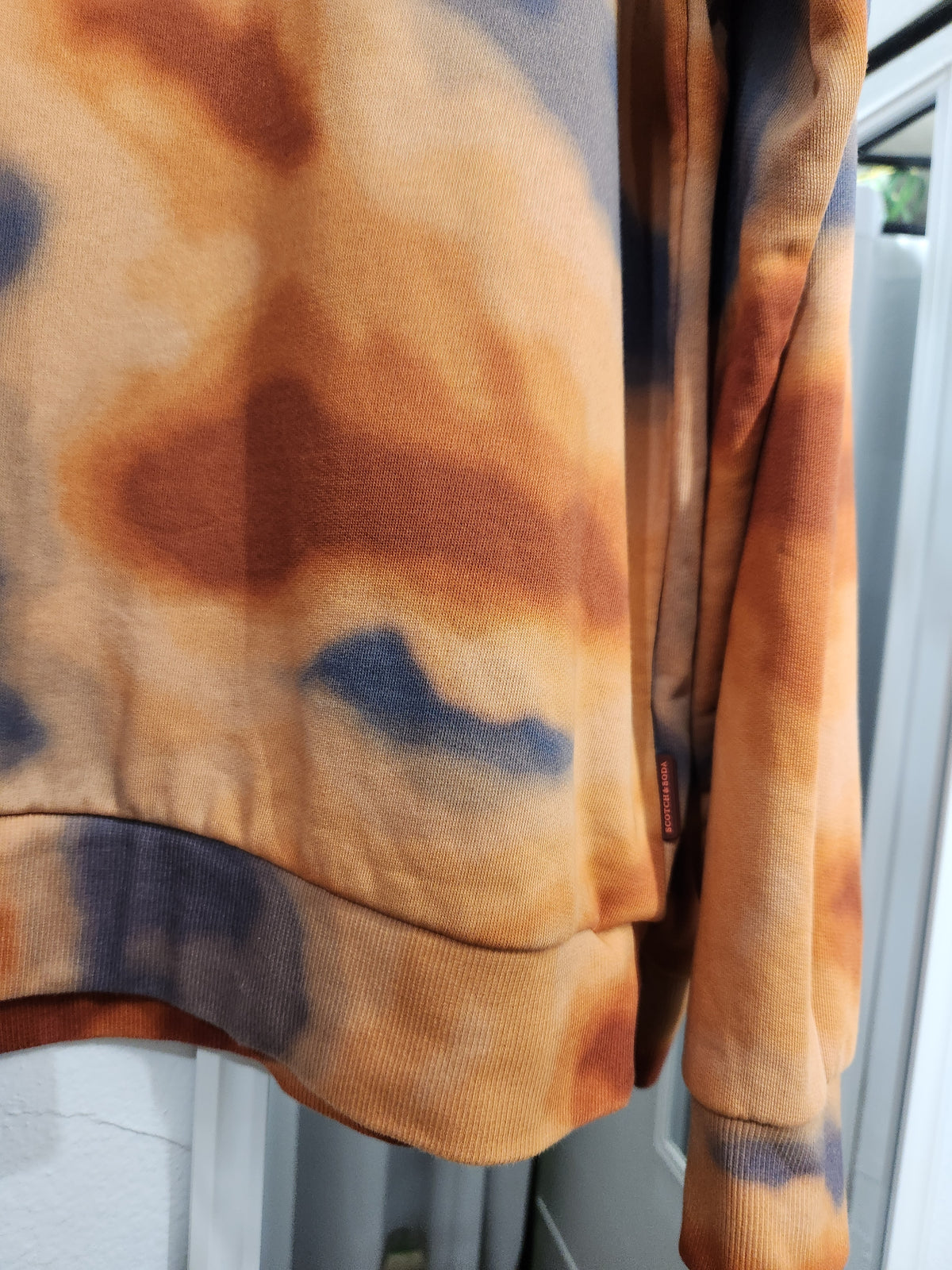 Close-up of a tie-dye sweatshirt in orange, brown, and blue, showing the ribbed hem and sleeve cuff.