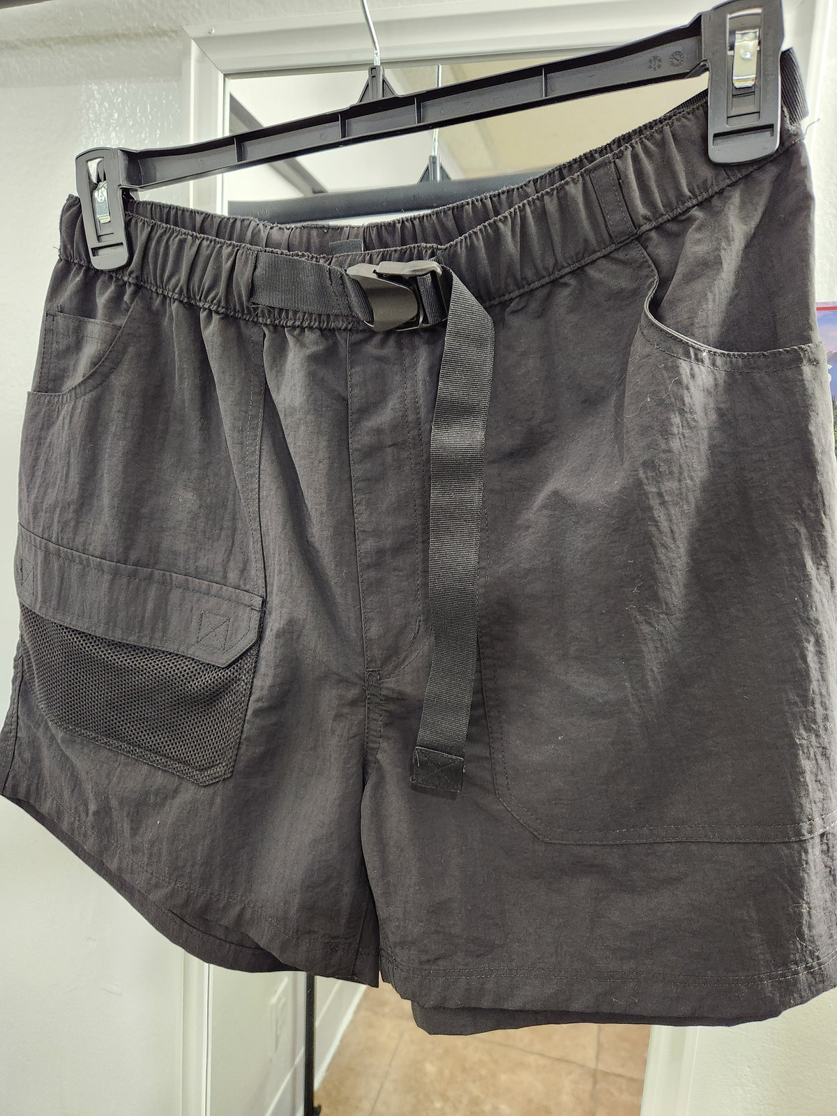 Dark gray cargo shorts with an elastic waistband and a matching fabric drawstring, hanging on a black hanger in front of a white door.