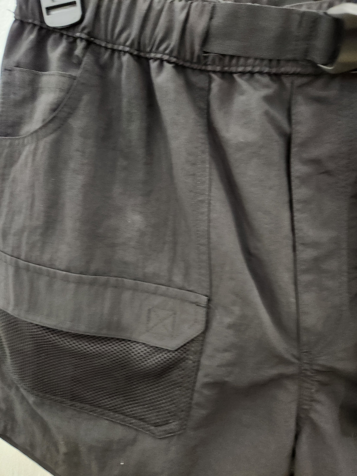 Close-up of dark gray outdoor shorts showing the elastic waistband, side pocket, and mesh pocket detail.