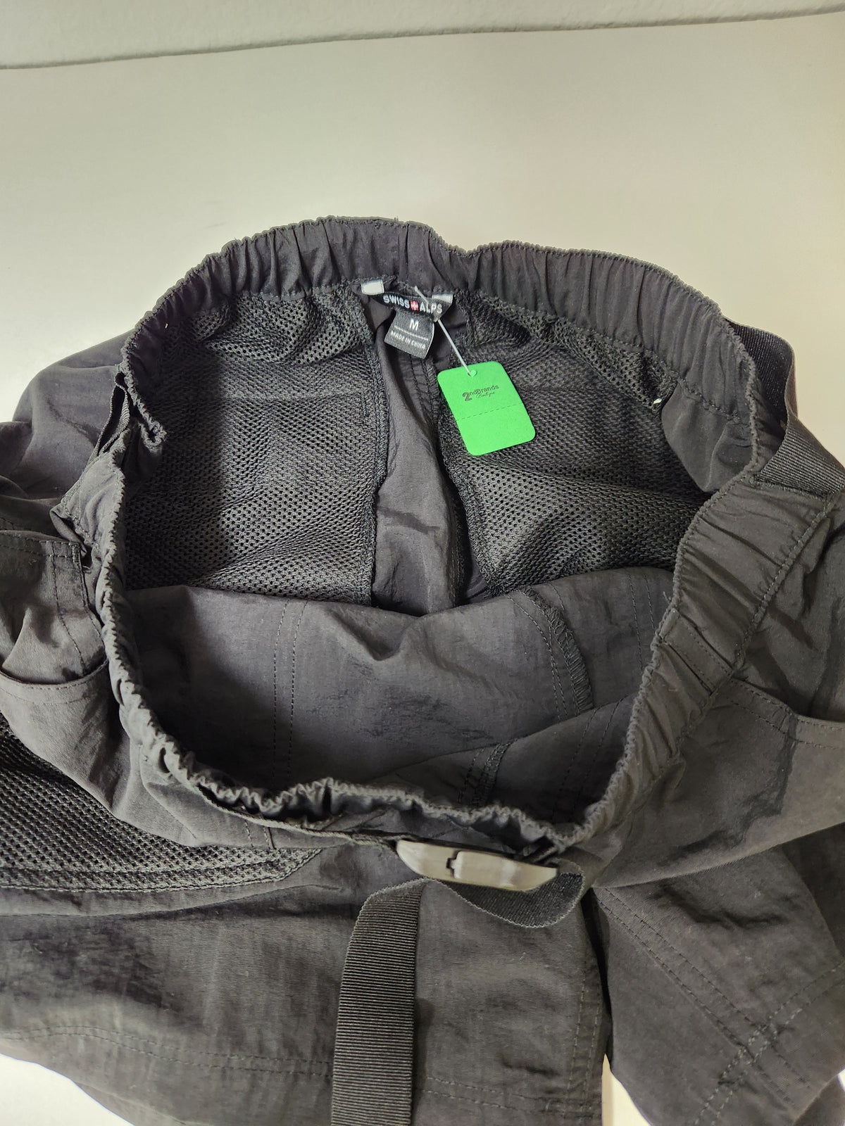 Close-up of the inside of a dark gray or black mesh garment, showing elasticized openings, interior fabric, and a bright green hangtag.